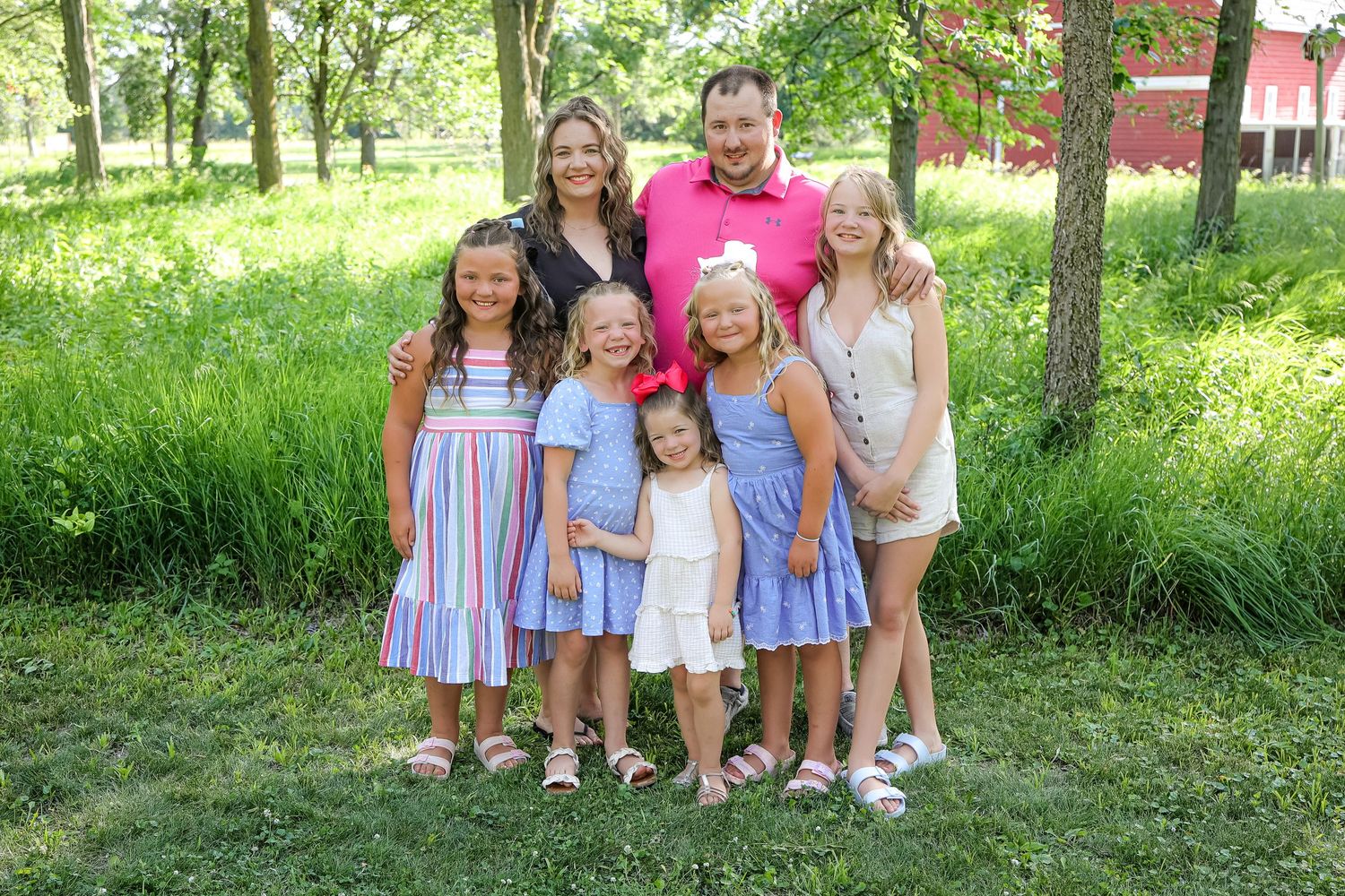 Family group poses outdoors in coordinated summer clothing against a lush green background.