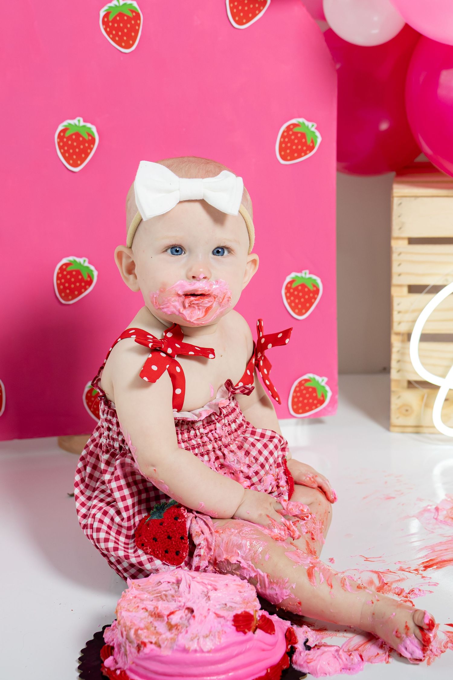 Messy cake smash photography scene with pink frosting and strawberry themed decorations.