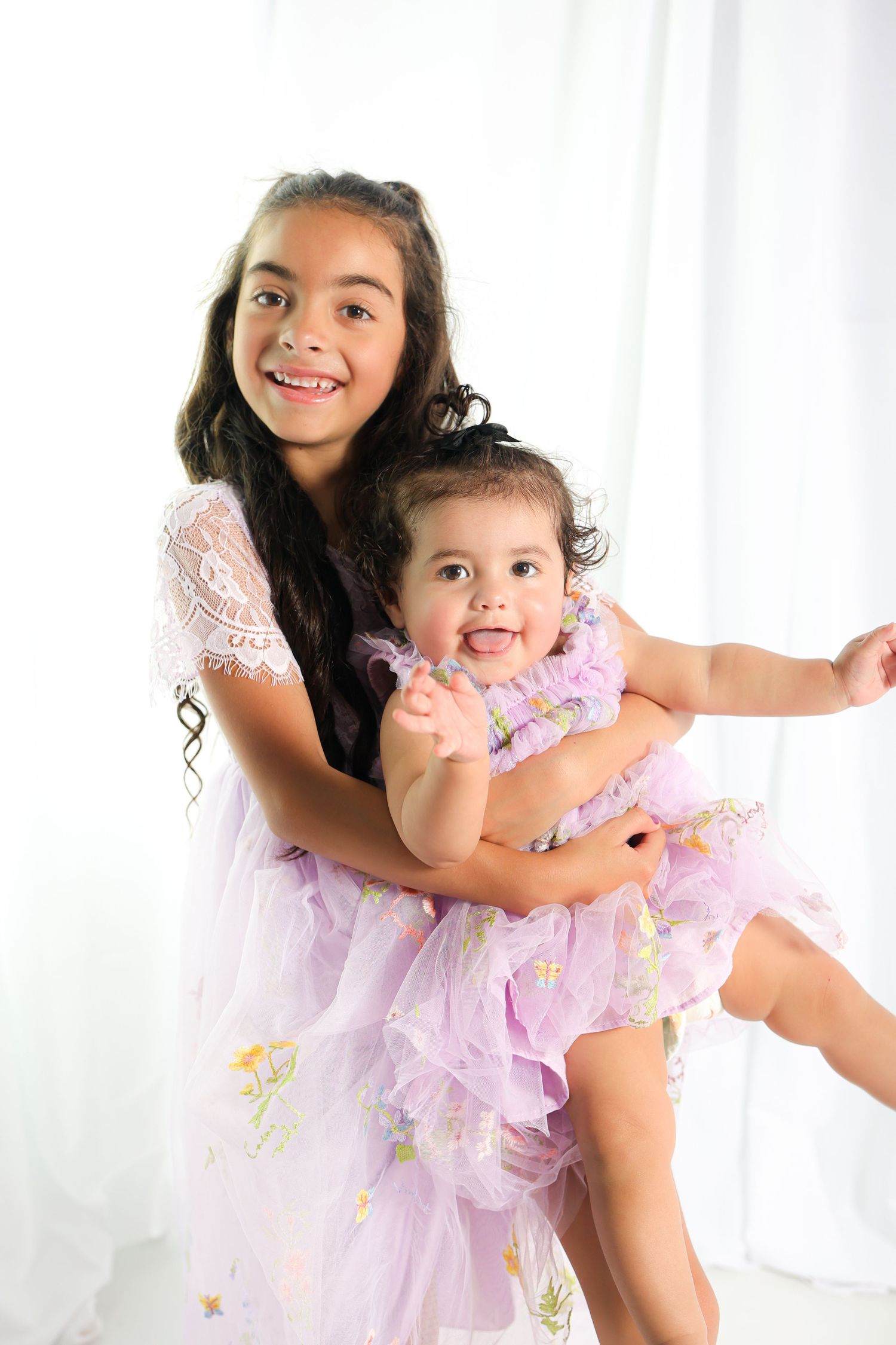 Two people in matching pink tulle dresses share joyful moment against white backdrop.