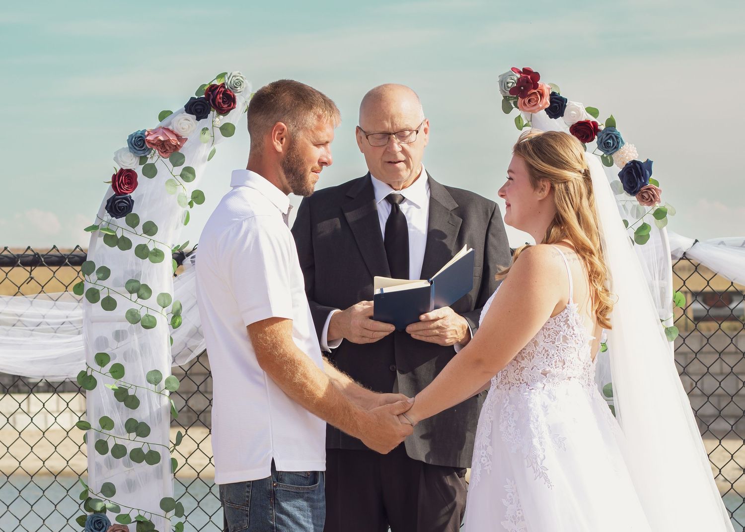 Wedding ceremony under blue sky with floral decorations and officiant.
