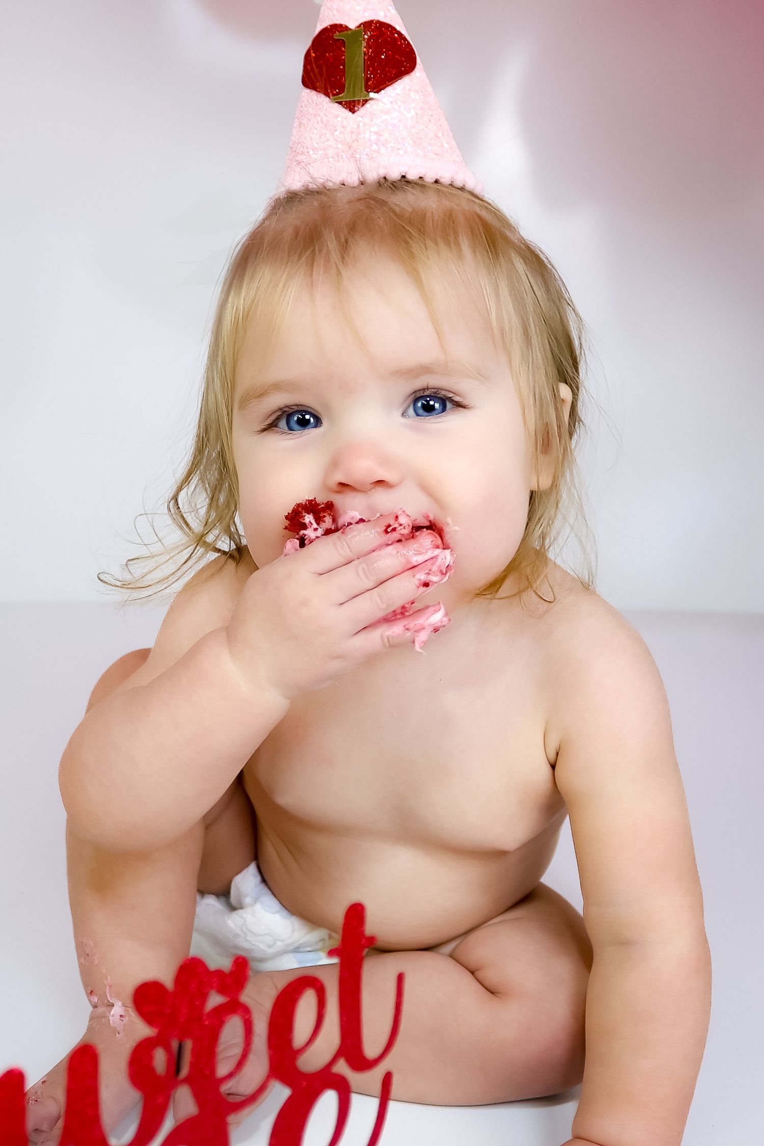 A toddler in a diaper enjoying red strawberries with messy face.