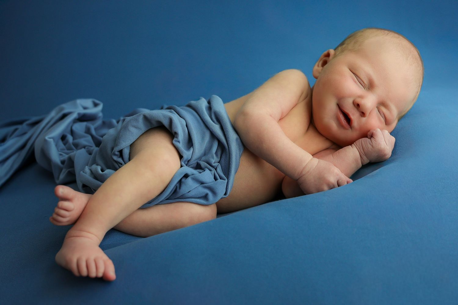 A sleeping newborn baby in blue swaddle cloth photographed from multiple angles against a dark blue background.