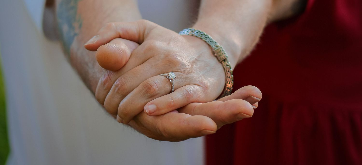 Two hands clasped together showing engagement rings against a soft background.