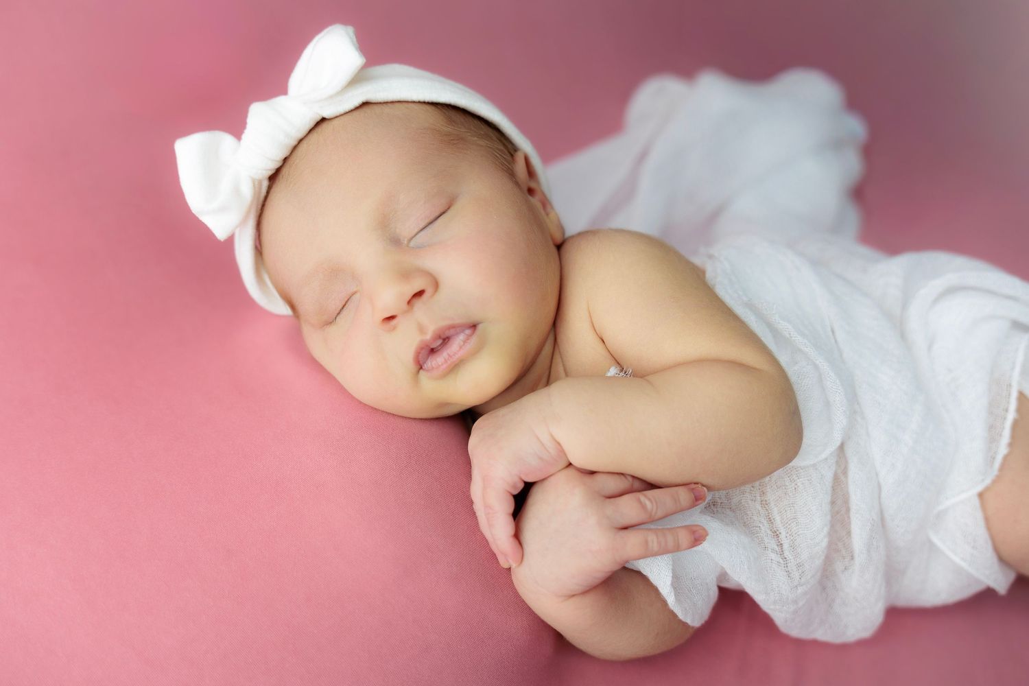 Sleeping baby in white clothing lies peacefully on pink background in series of connected photos.