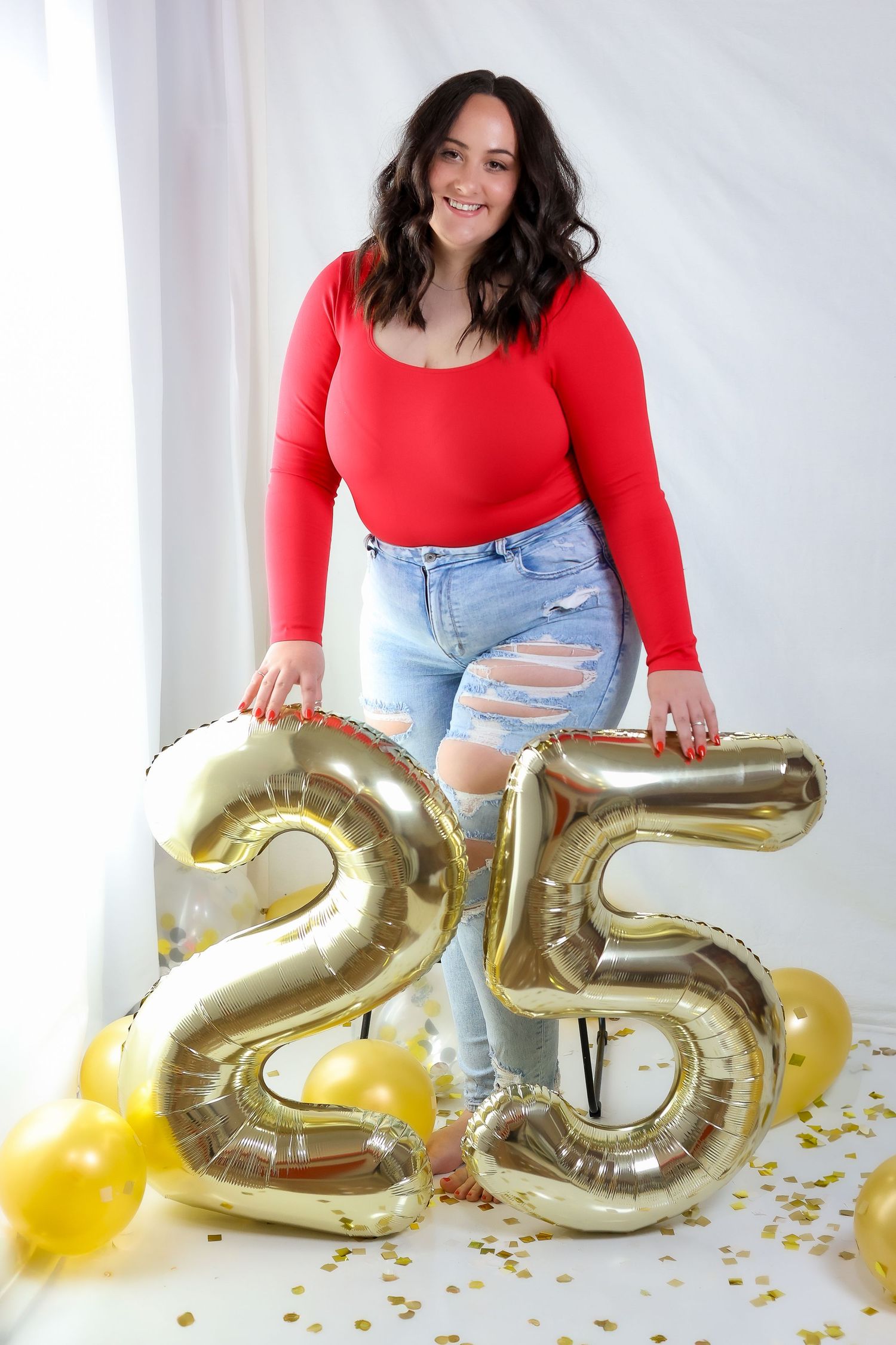 Large gold number 25 balloons with yellow decorations on a white backdrop.