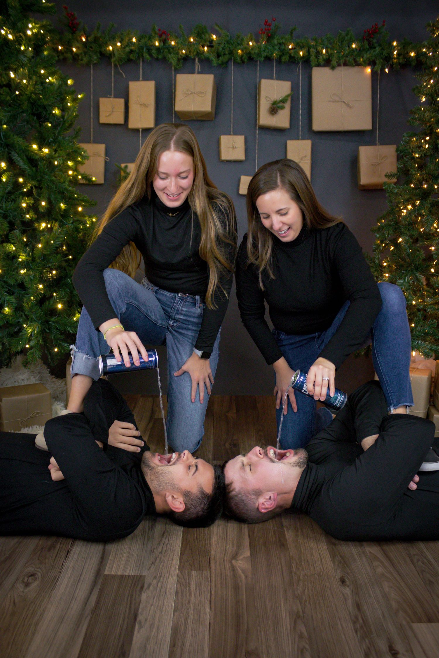 Playful family photo session with fun poses on hardwood floor by Christmas tree.