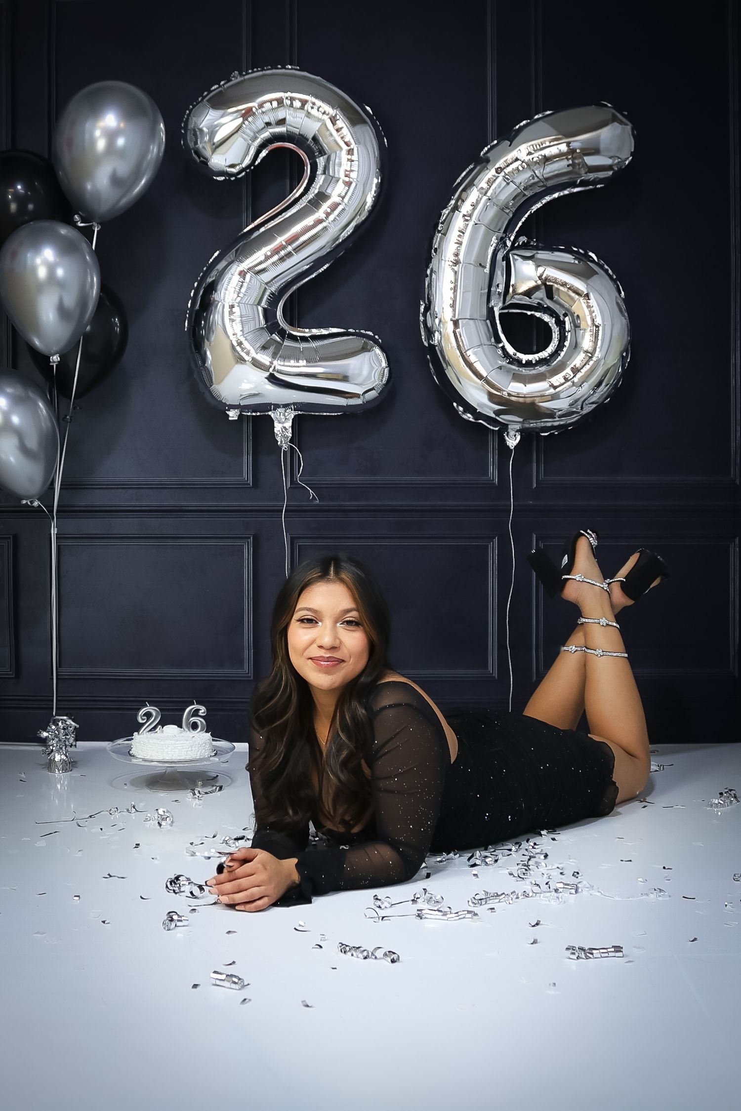Birthday photoshoot setup with silver number balloons and confetti on dark background.