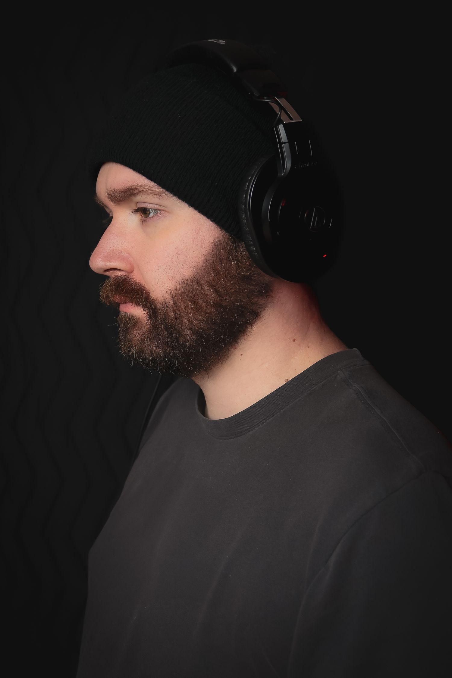 Side profile of person wearing headphones and beanie against dark background.