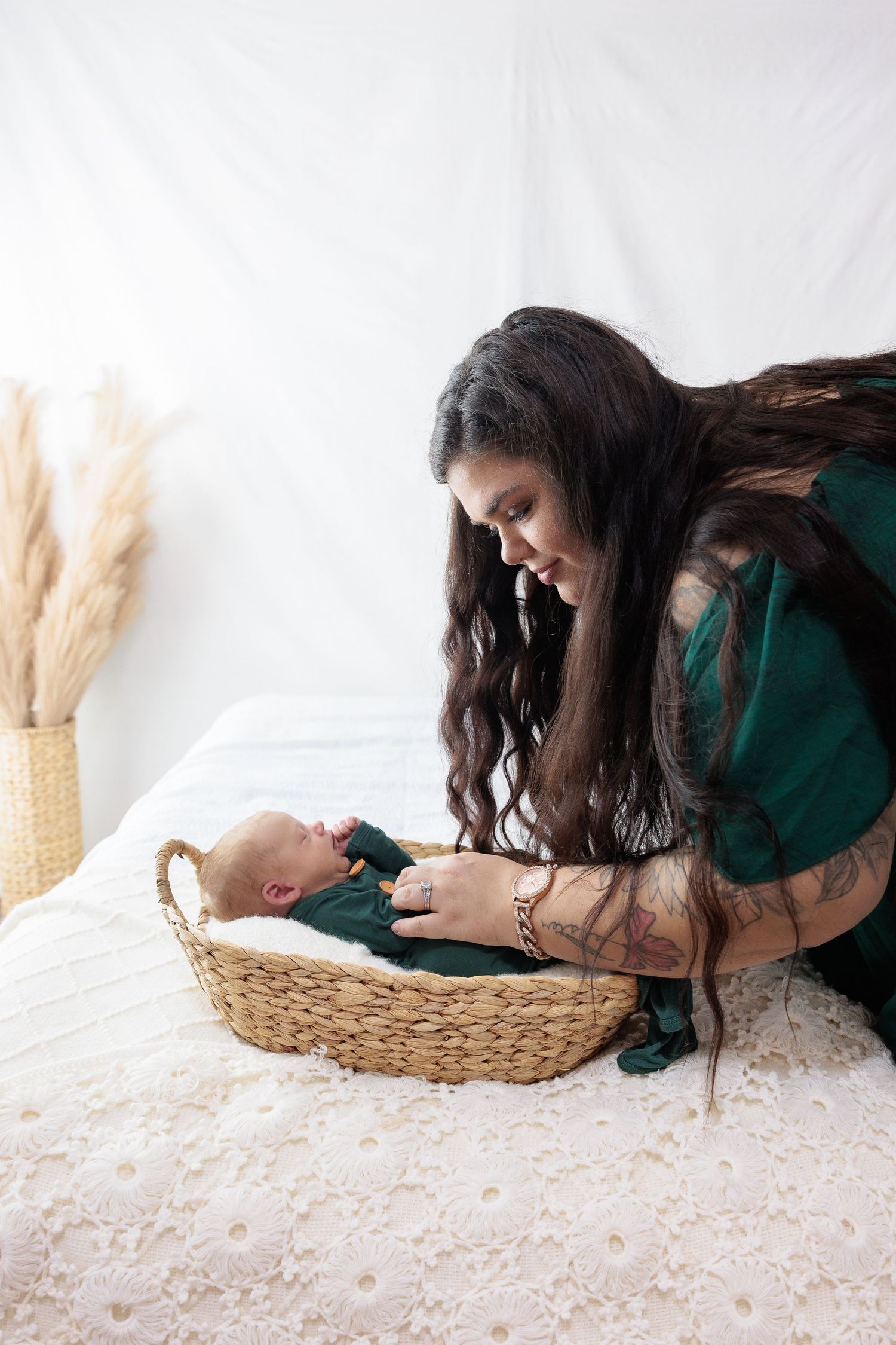 A woman in a green dress leans over a woven basket containing a small baby.