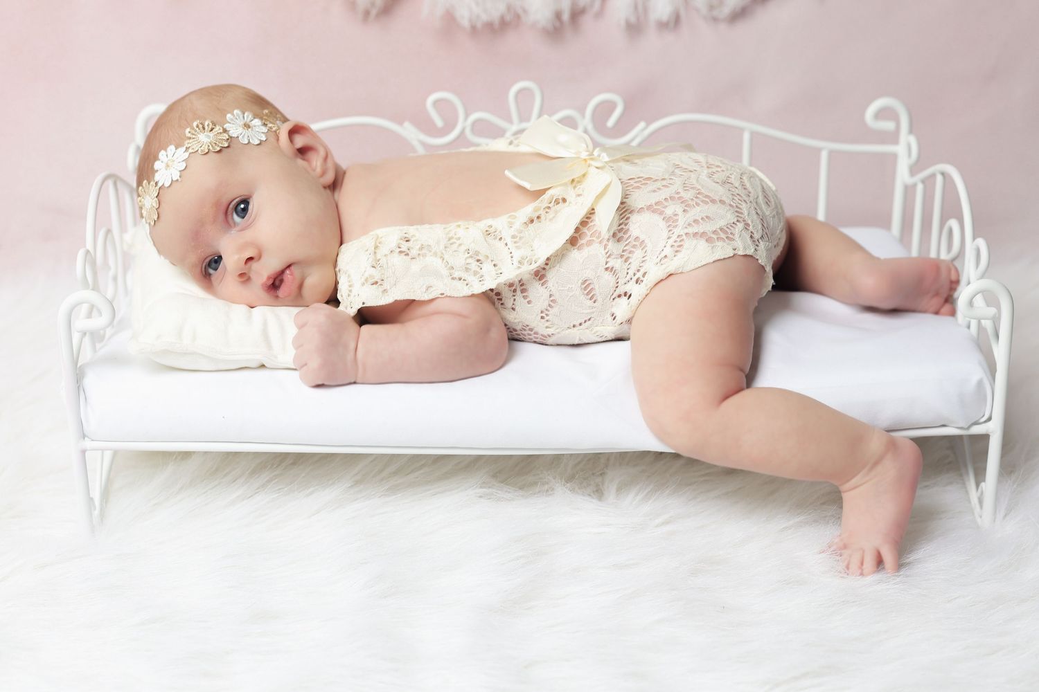 Baby in lace outfit resting on decorative white metal bed frame.