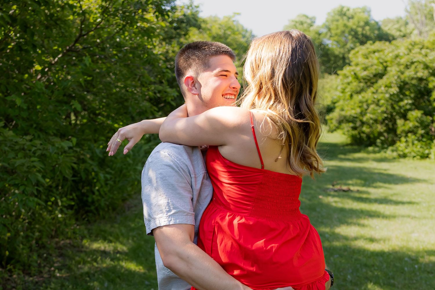 Couple embracing outdoors in park with lush green summer foliage.