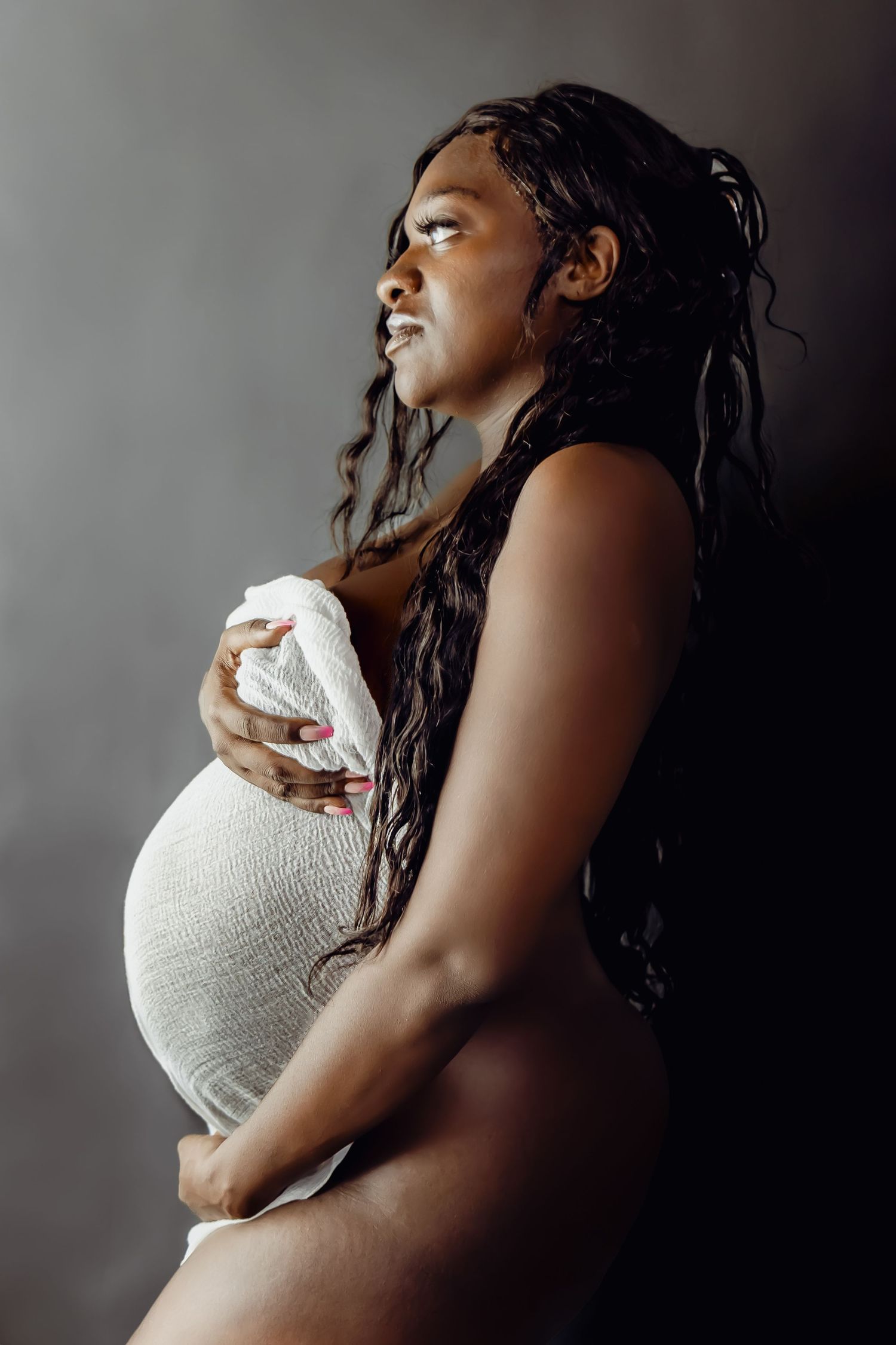 Elegant maternity photo with dramatic lighting and flowing hair.