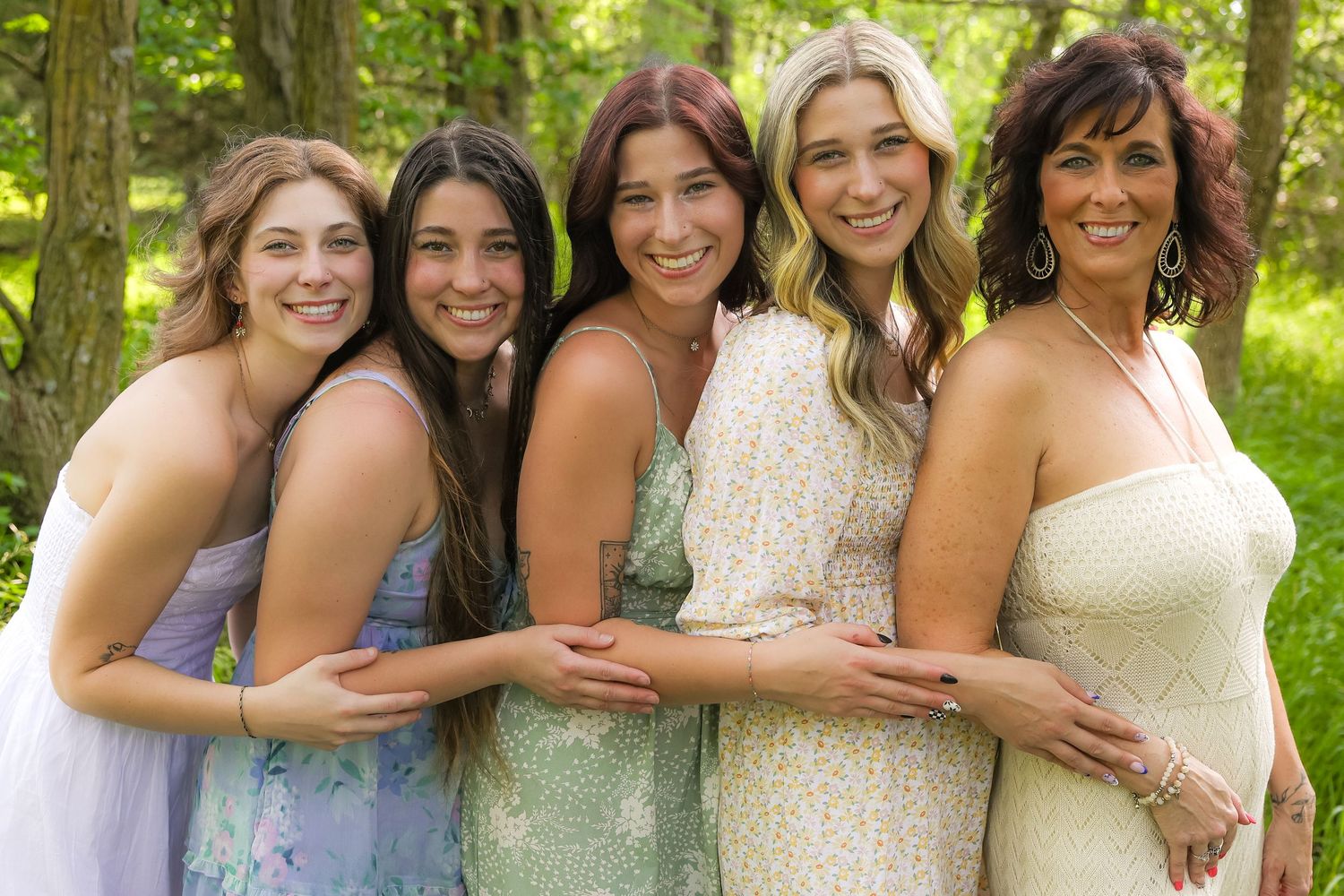Group portrait of people wearing light colored dresses in a sunny woodland.
