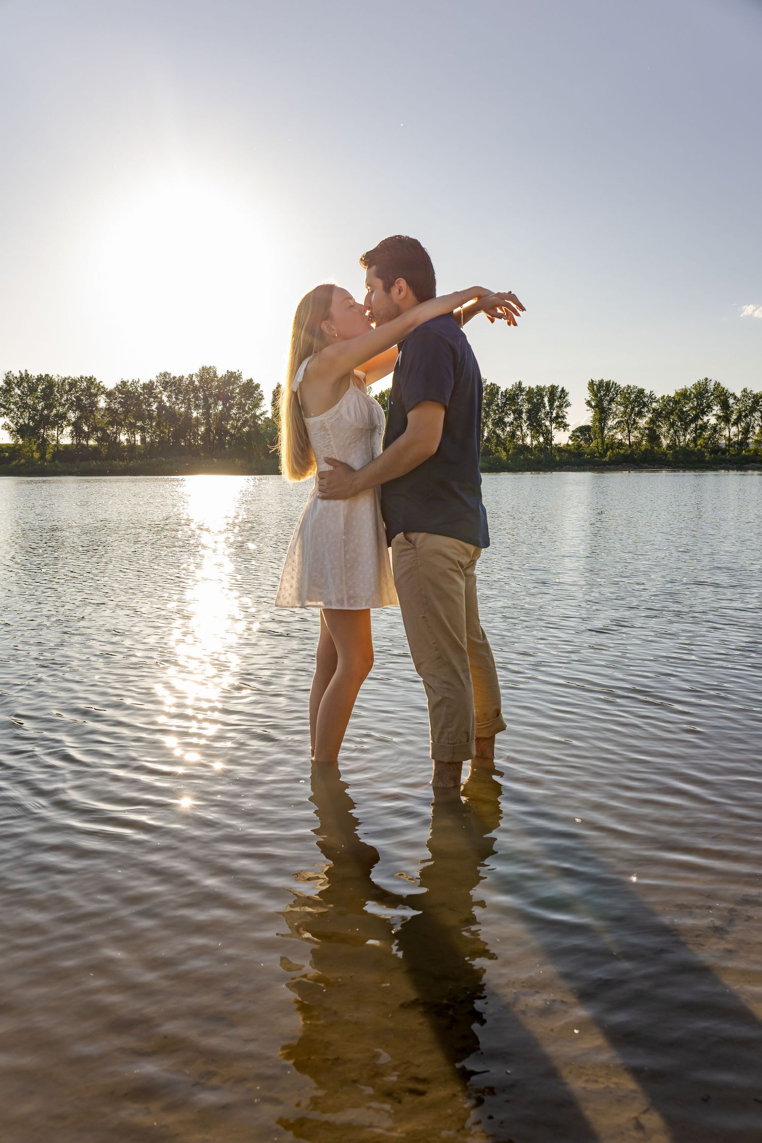 Couple embracing in lake water during golden hour with sun reflecting on rippling surface.