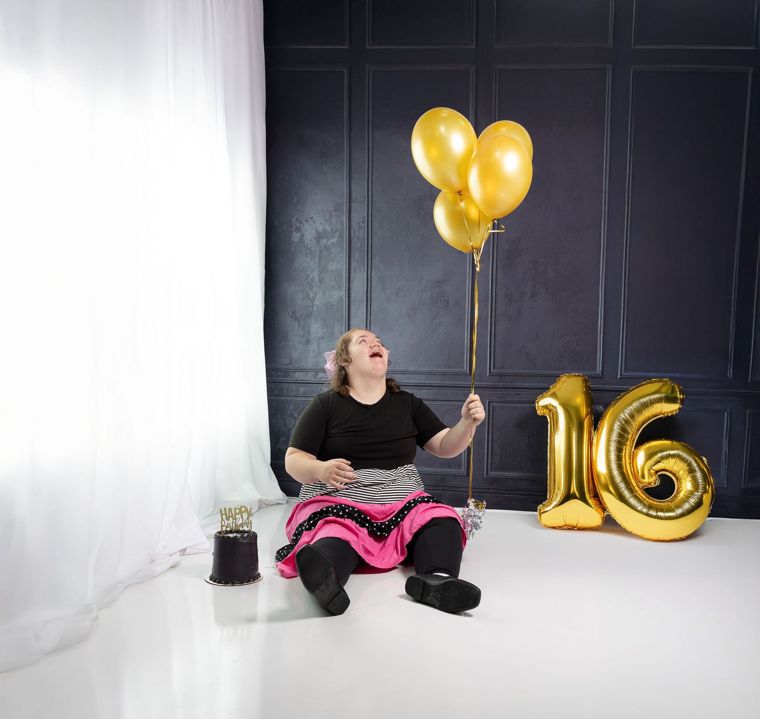 A creative photo collage showing a person sitting against a dark wall with gold balloons and pink decor elements.