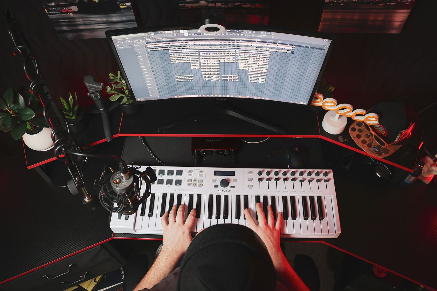Close-up view of hands playing on illuminated electronic keyboard keys in dark studio setting.