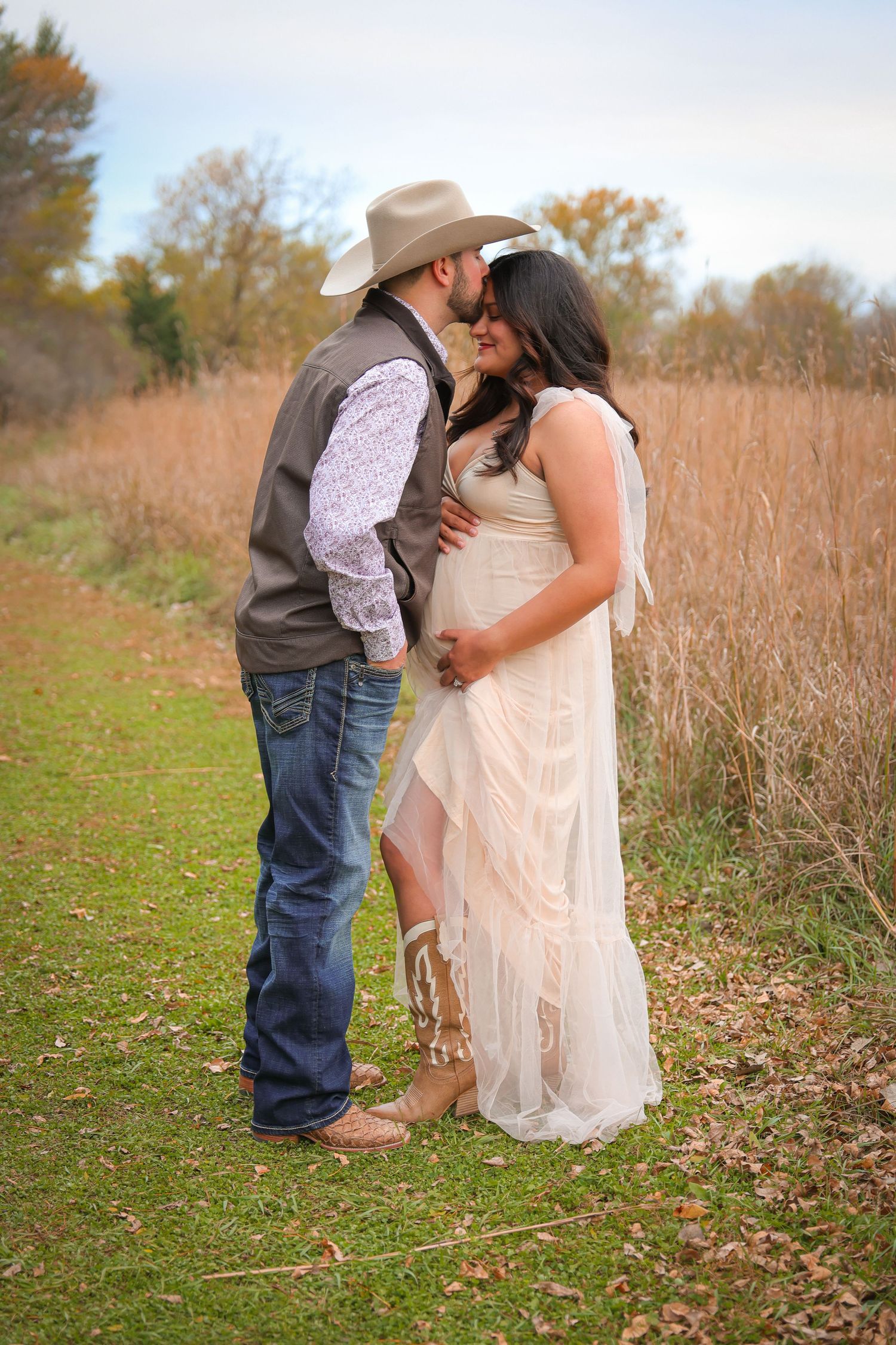 A couple shares an intimate moment in a rustic autumn field with tall grass and fallen leaves.