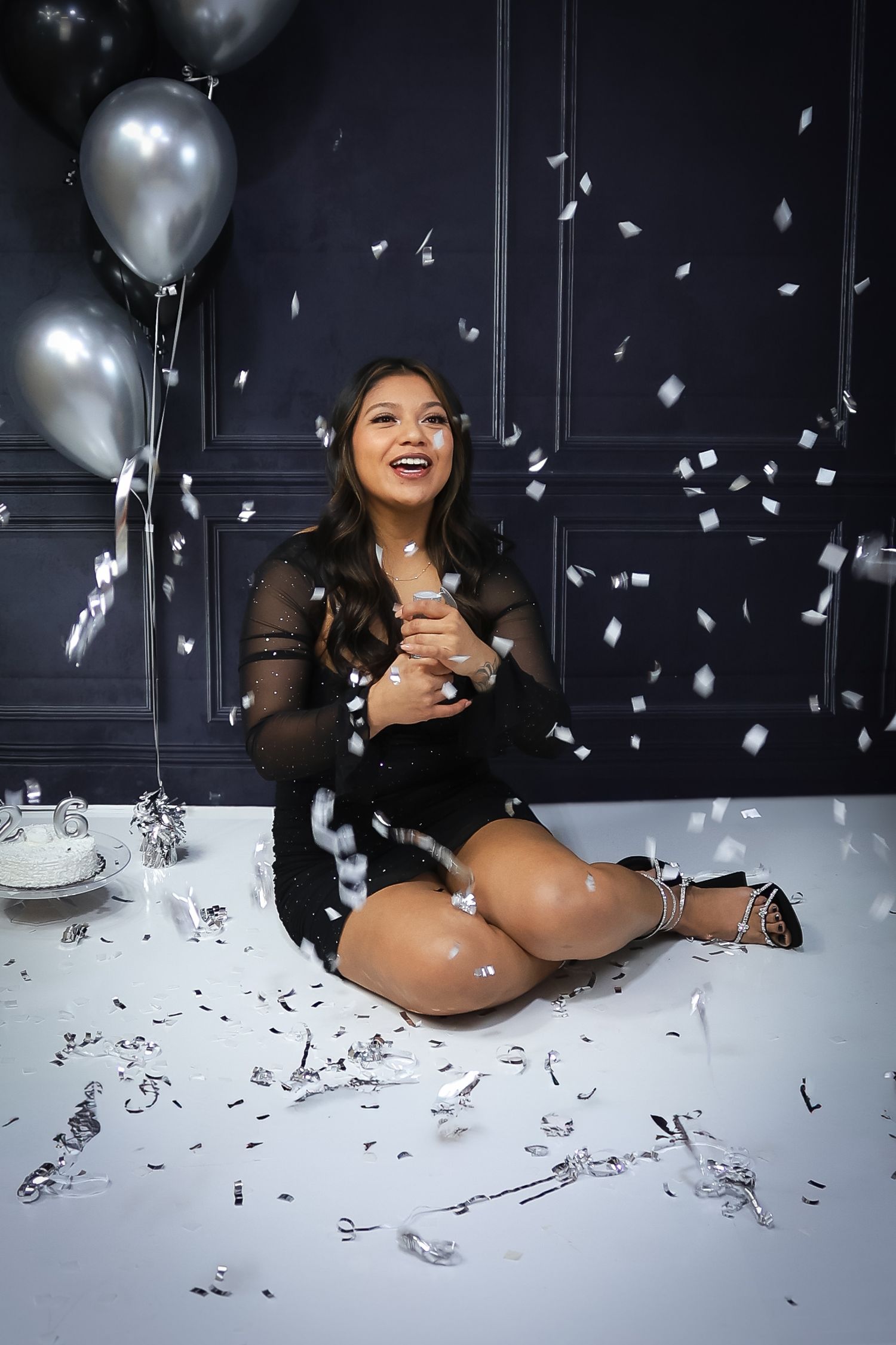 Glamour photoshoot with silver balloons and confetti against dark background.