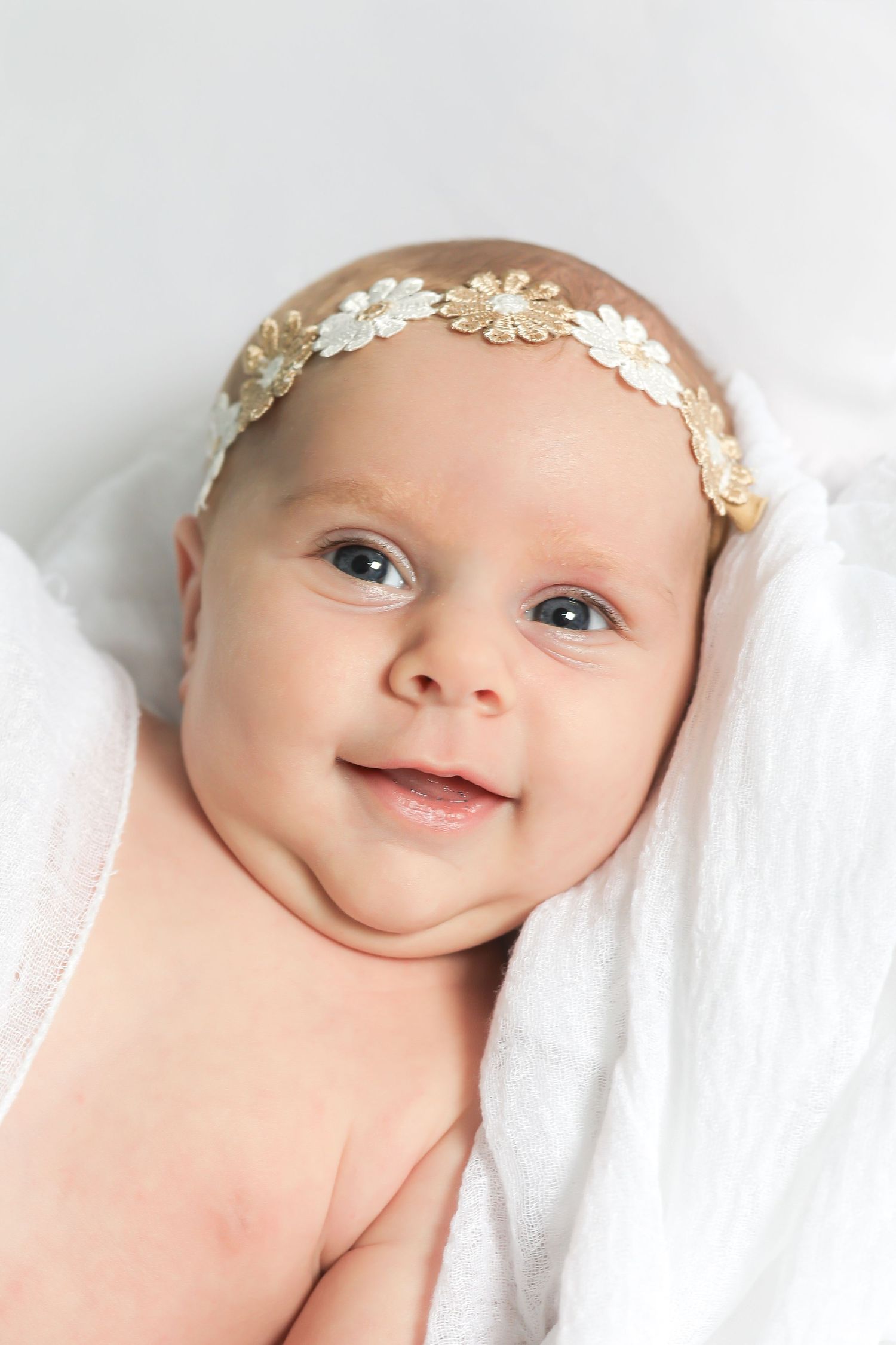 Baby wearing delicate floral crown headband against white background.