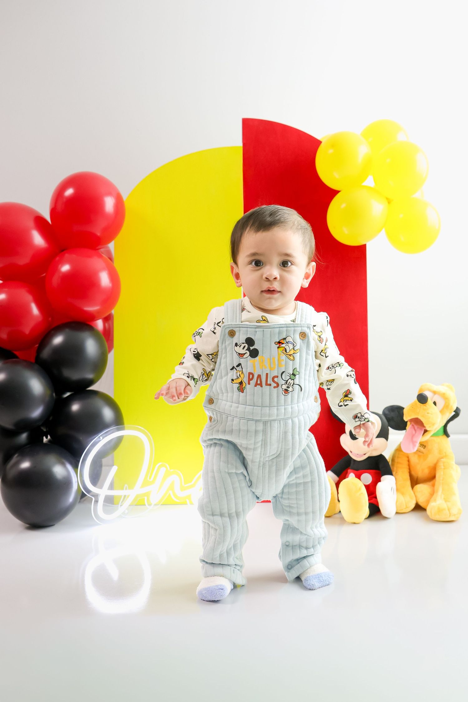 Mickey Mouse themed first birthday party setup with red, yellow and black balloons and decorative plush toys.
