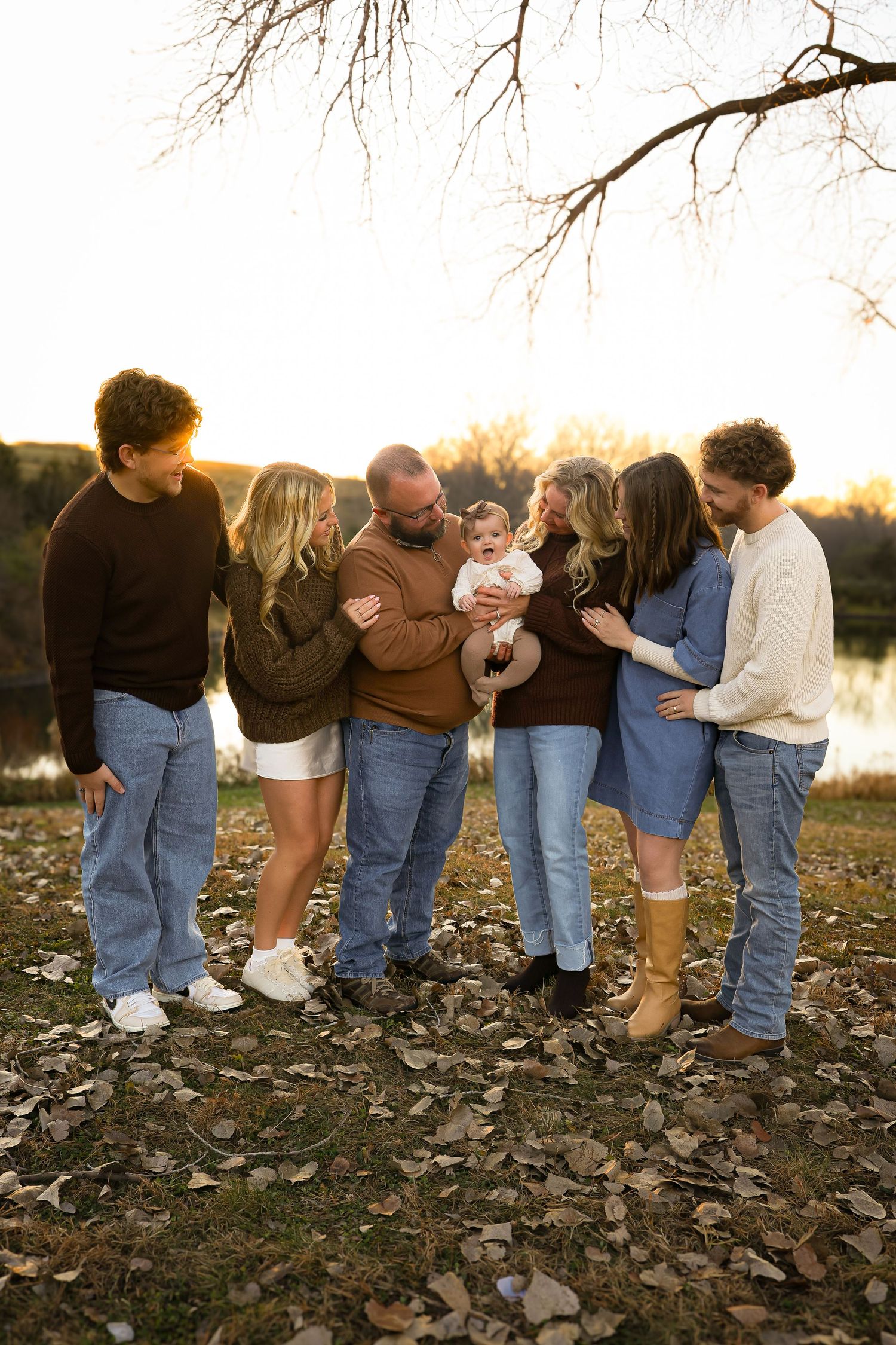 A creative family photo sequence showing people bending down to look between their legs at sunset by a lake.