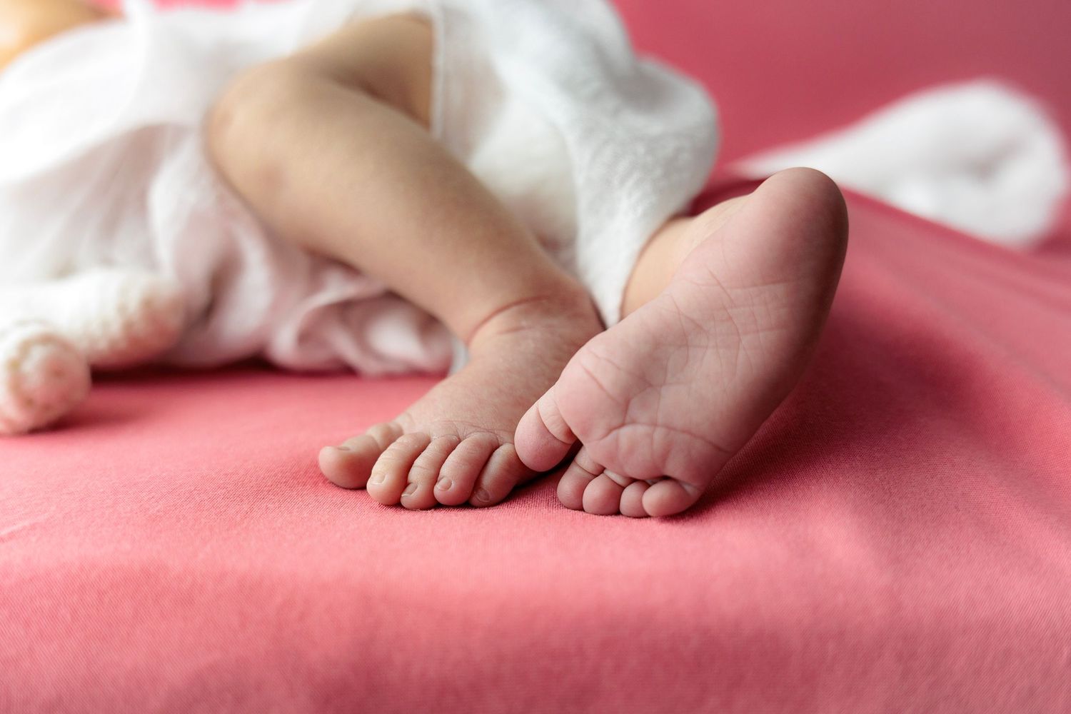 Close-up of tiny newborn baby feet on soft pink fabric creating a tender and gentle nursery scene.