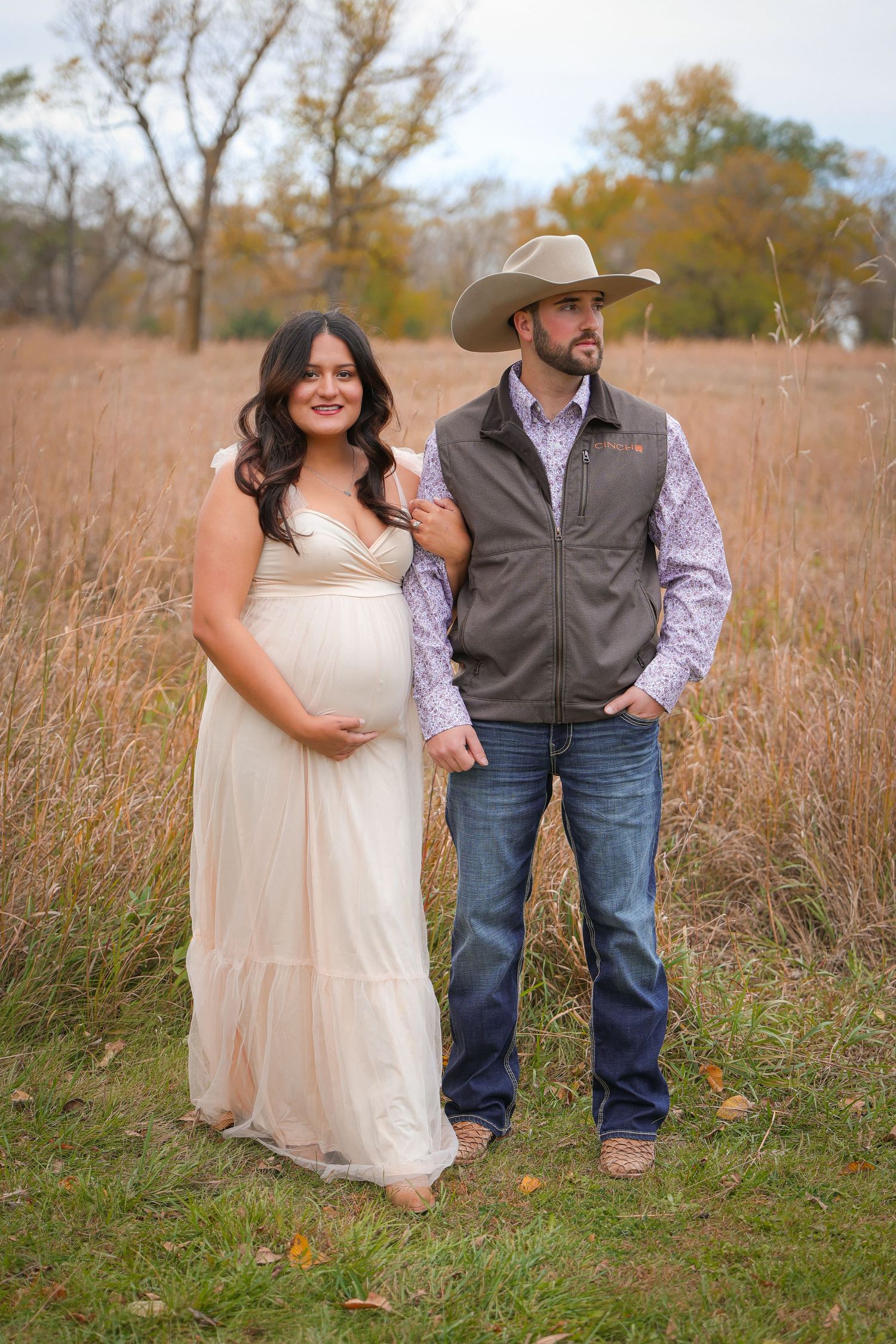 A couple poses together in a rustic autumn field with tall grass and warm golden lighting.