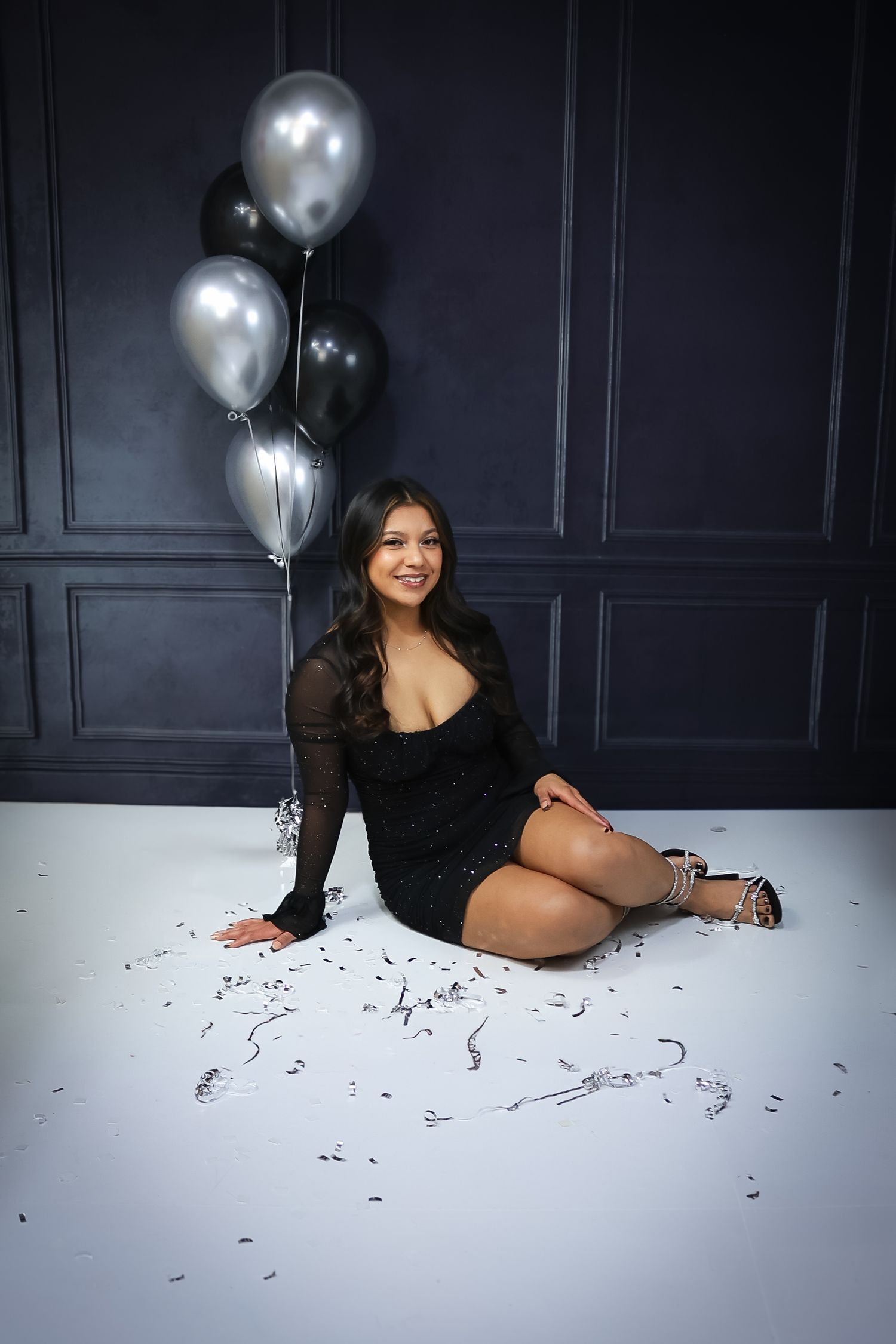 Studio photoshoot with silver and black balloons against dark paneled wall.