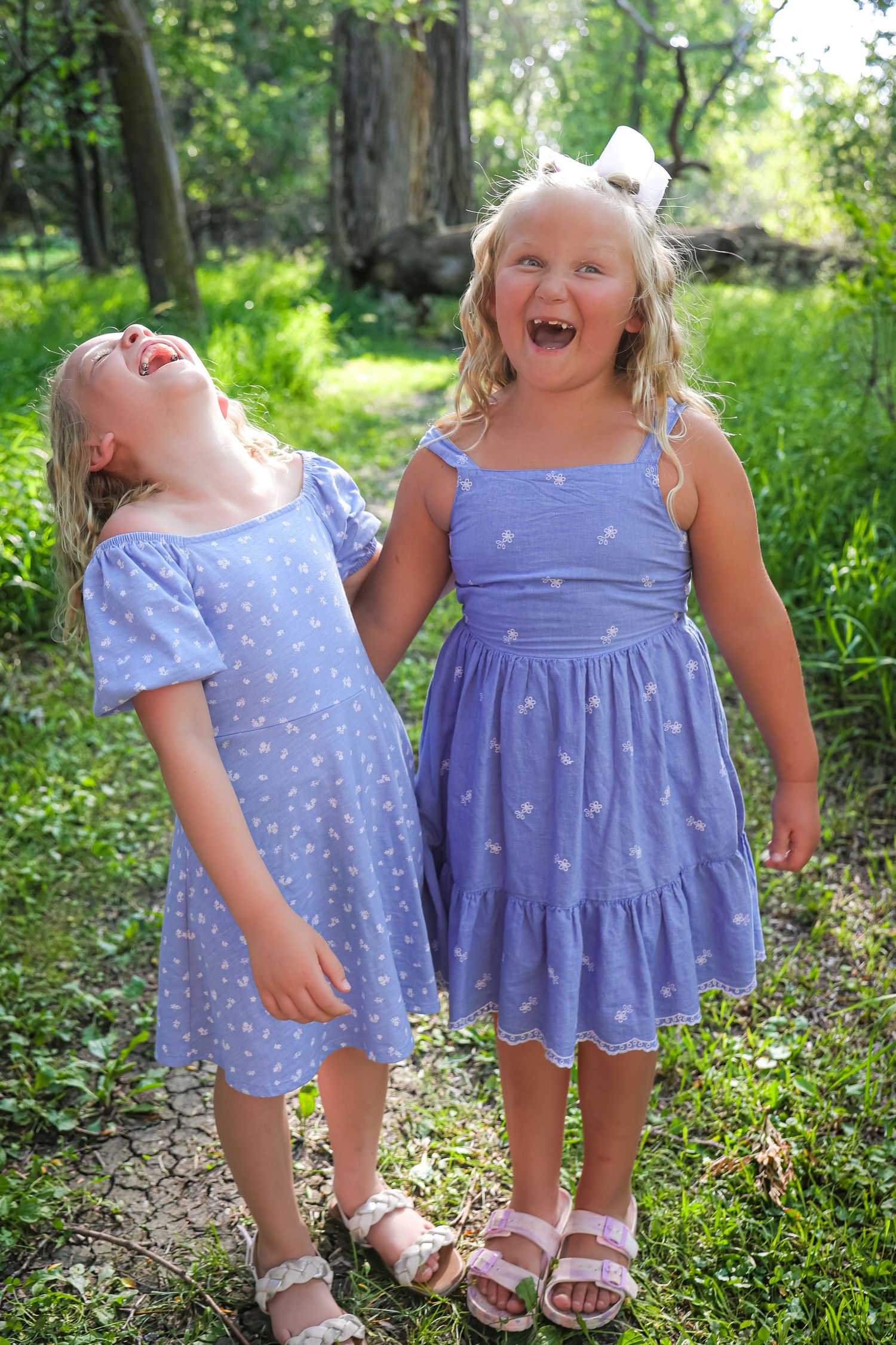 Children in matching purple dresses laugh and play together on woodland path.