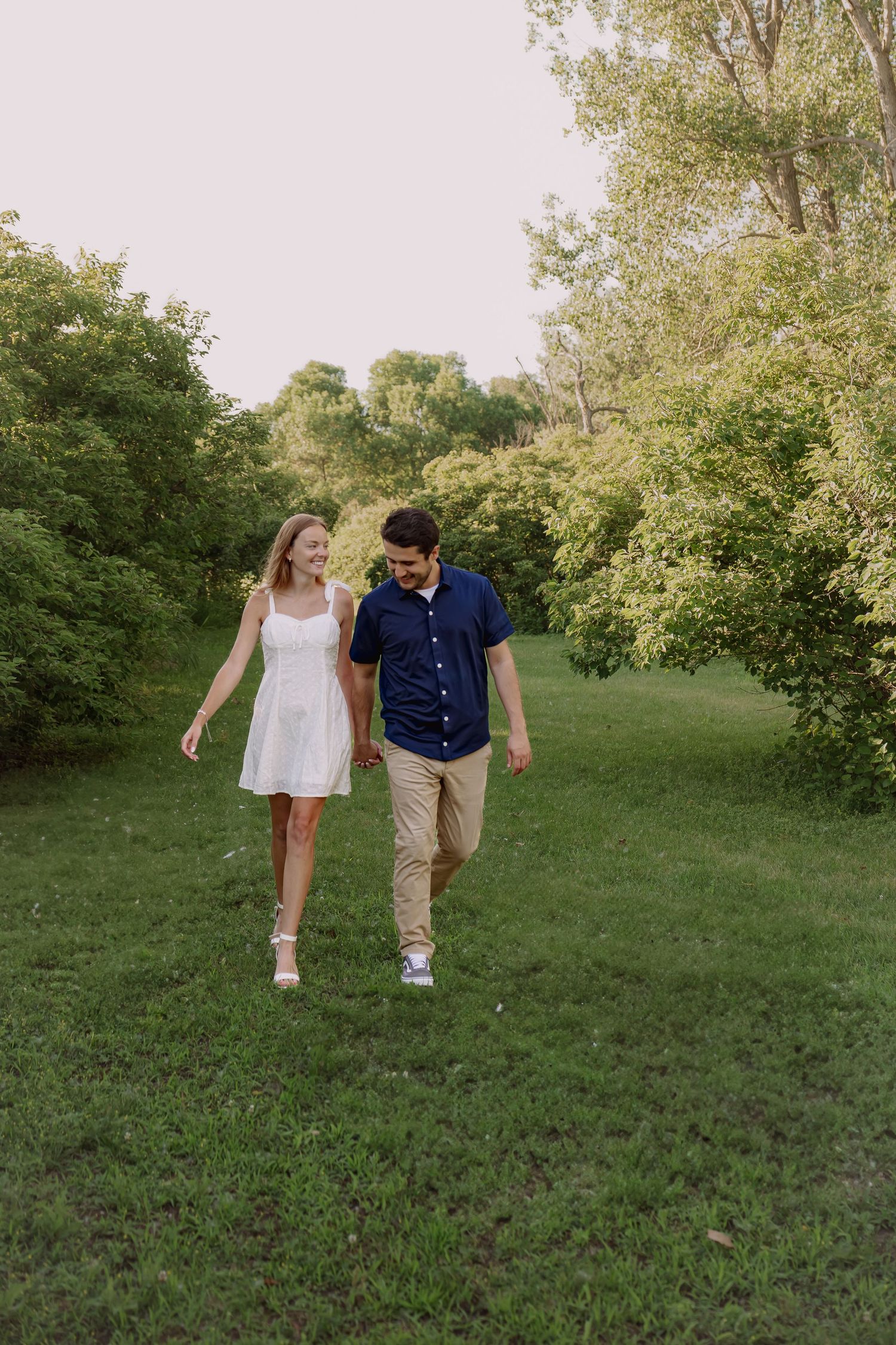 Couple walking together through lush green park setting.