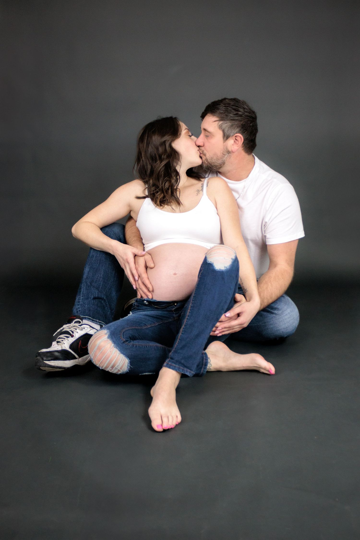 Intimate maternity photo series showing couple's tender moments on dark floor.