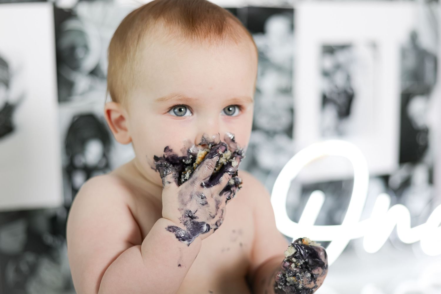A baby with messy hands and face enjoys a cake smash photoshoot.