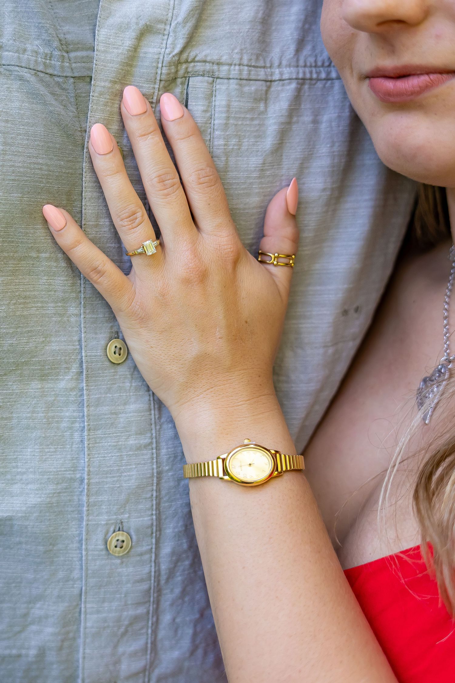 Close-up of hands showing gold jewelry including rings and watch against gray fabric.