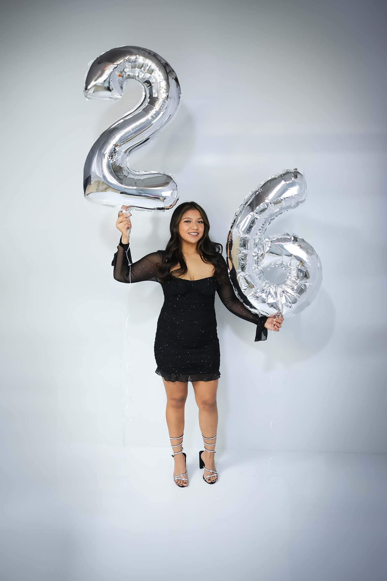 Celebratory photoshoot with large silver number balloons against light background.