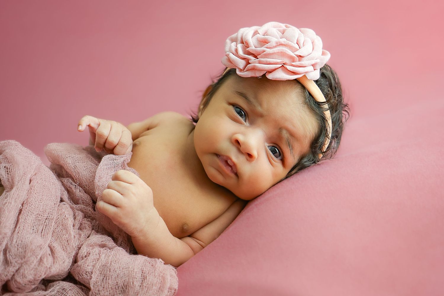 Sleeping newborn baby with dark hair lies on pink background in multiple artistic poses.