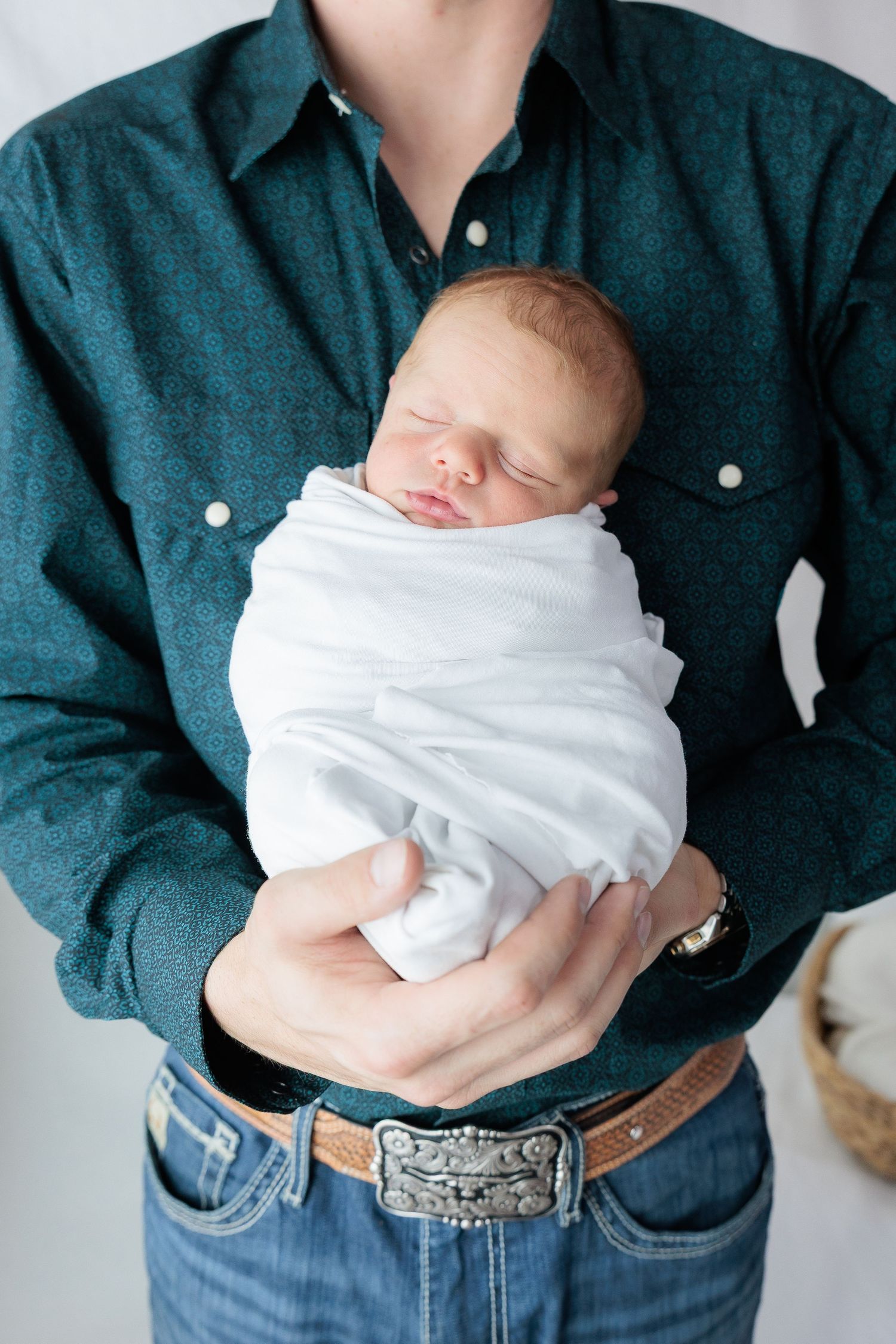 A series of four photos showing a baby swaddled in white being held against a dark blue denim shirt.