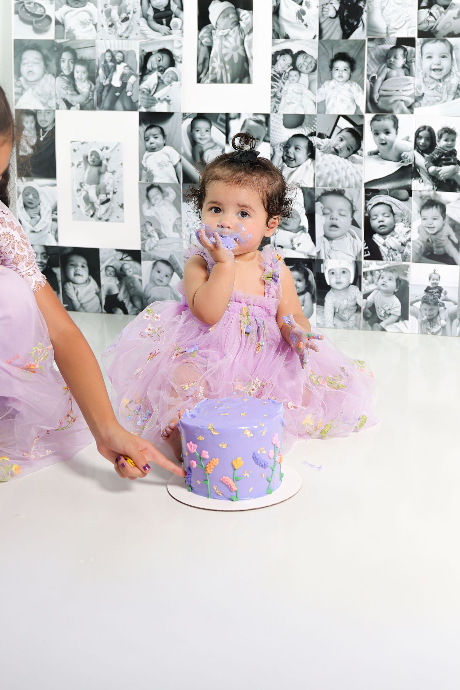 Baby in tulle dress tastes purple birthday cake during professional photoshoot.