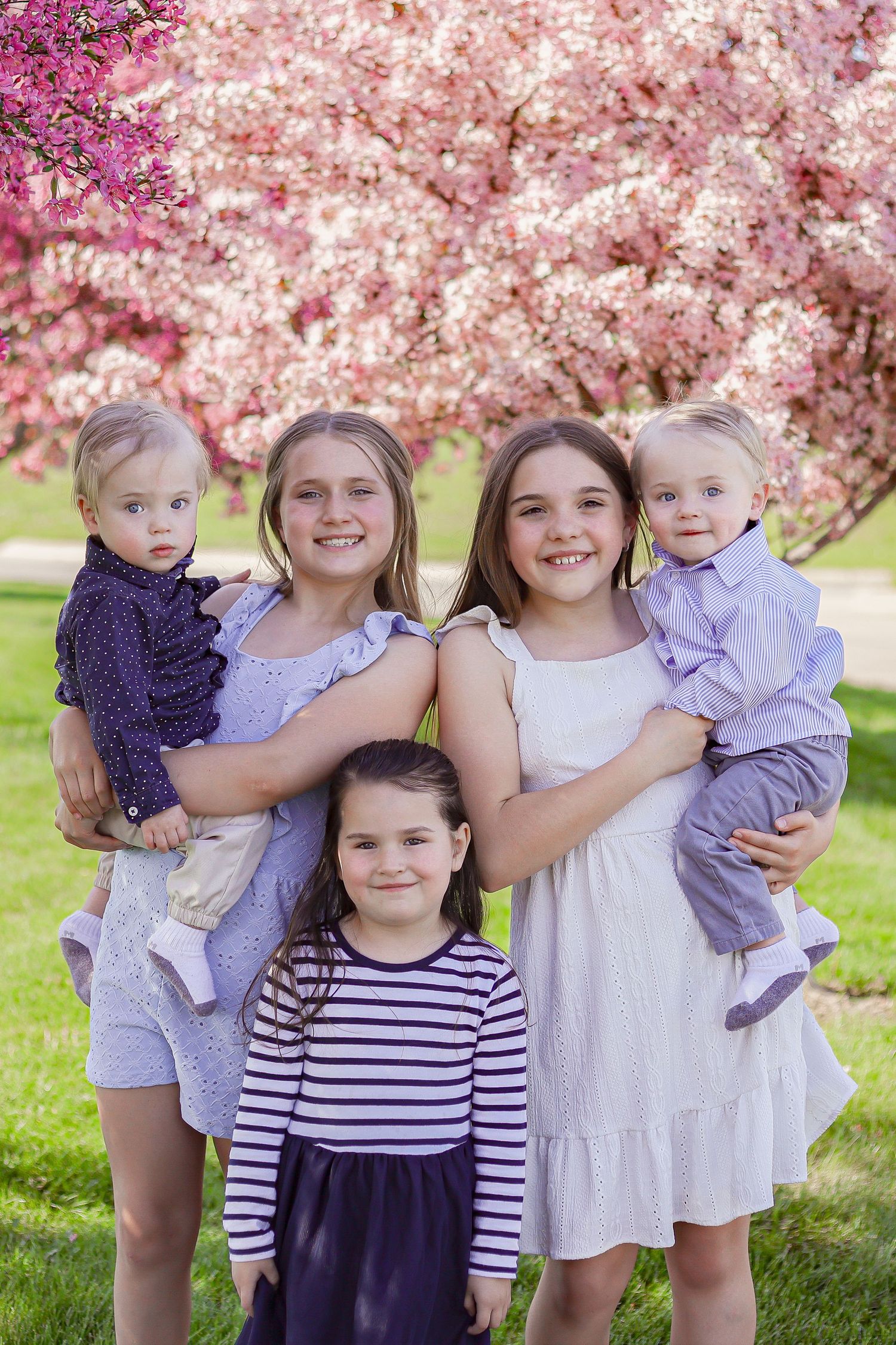 A group of children in coordinated navy and white outfits pose together under pink cherry blossoms.