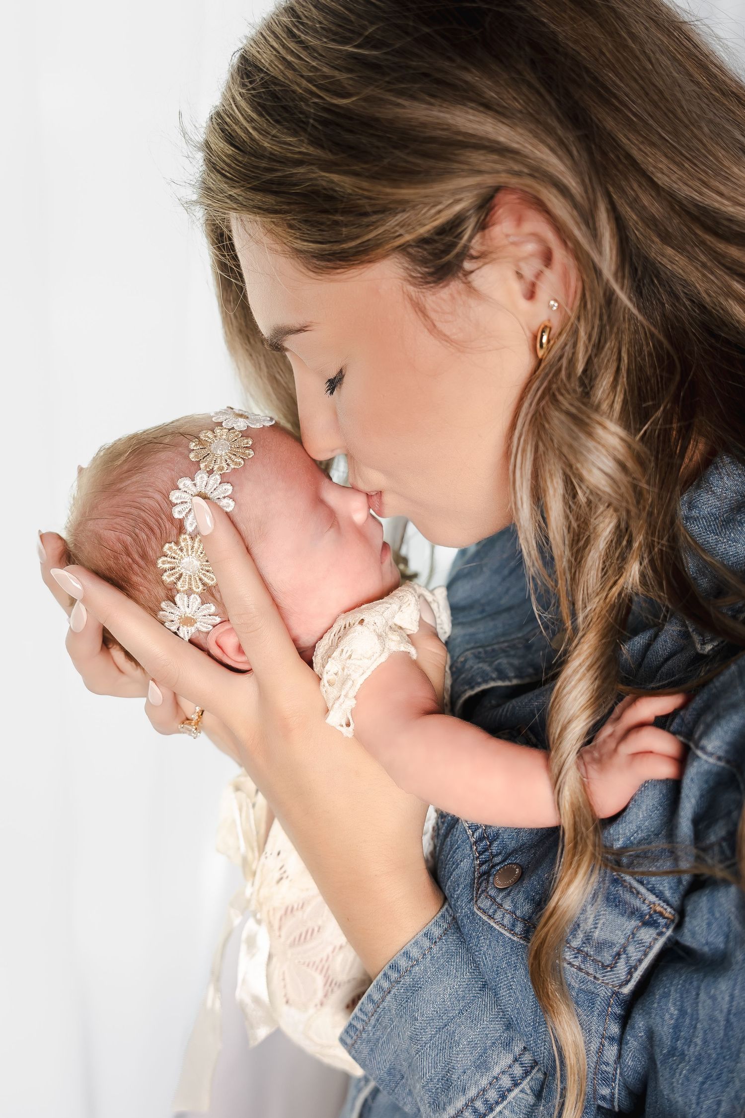 Tender moment between parent and newborn baby in denim jacket against white background.
