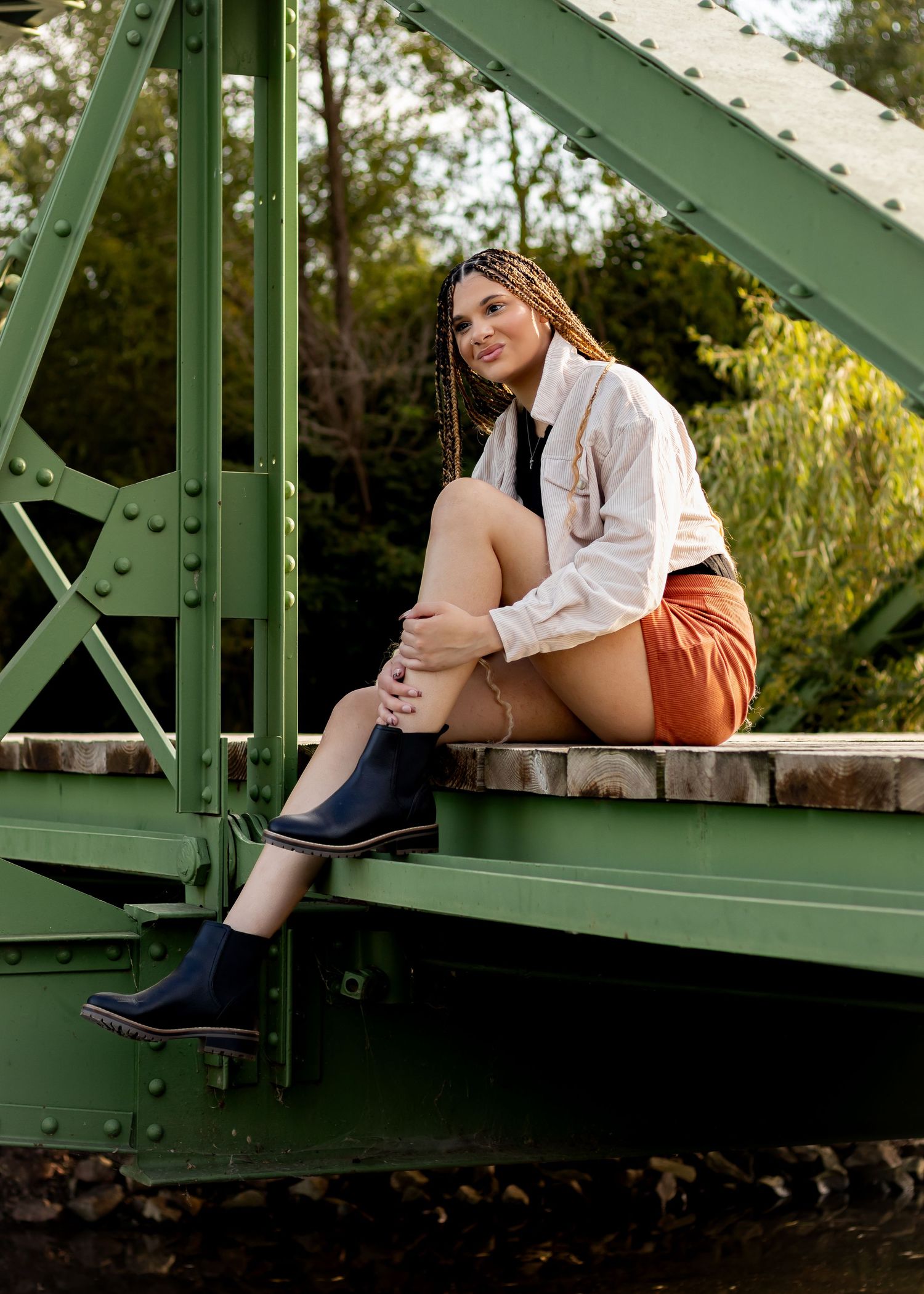 Fashion portrait on green metal bridge wearing white shirt and rust-colored shorts.