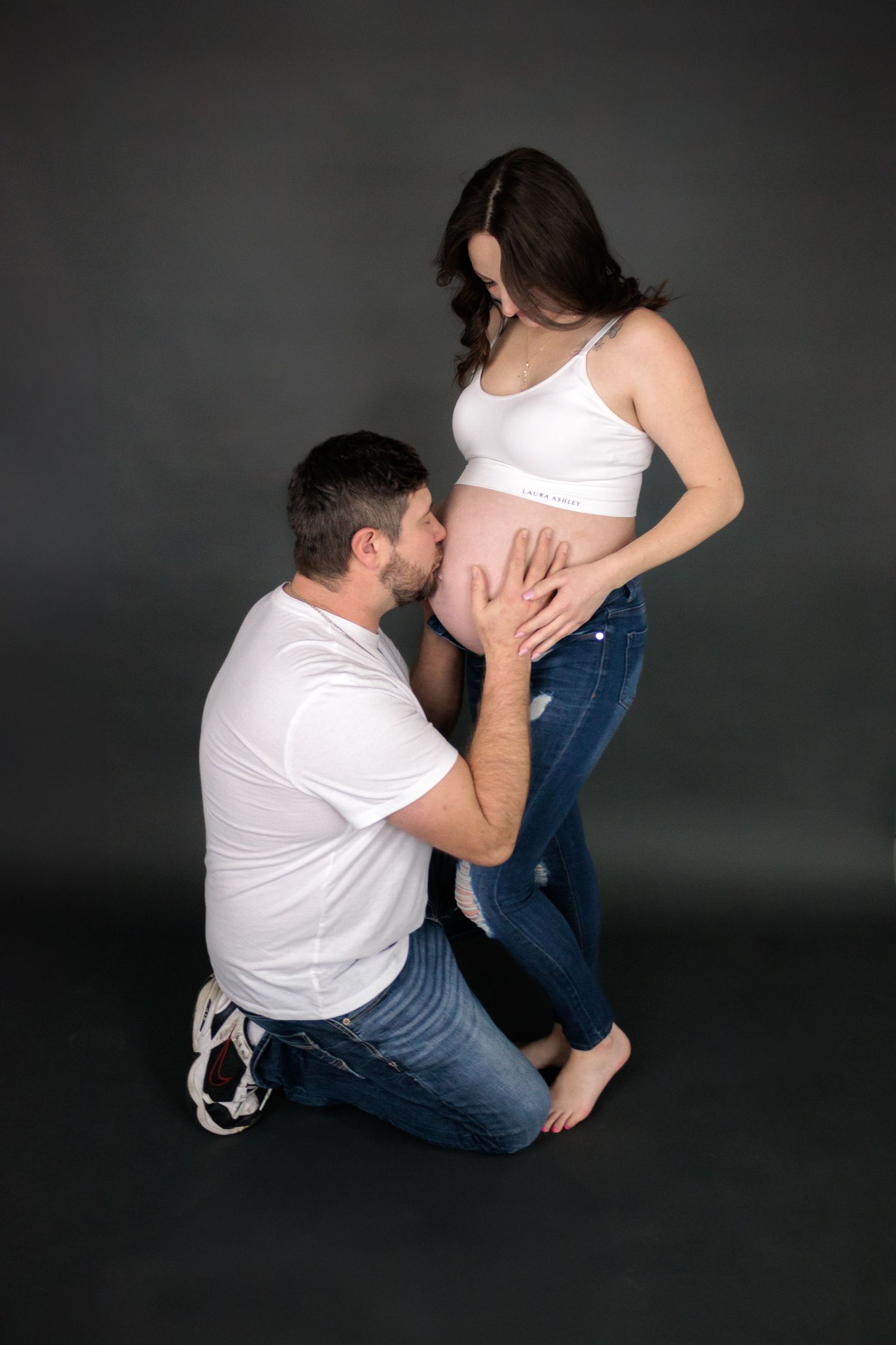 Intimate maternity photography sequence showing couple embracing on dark floor.