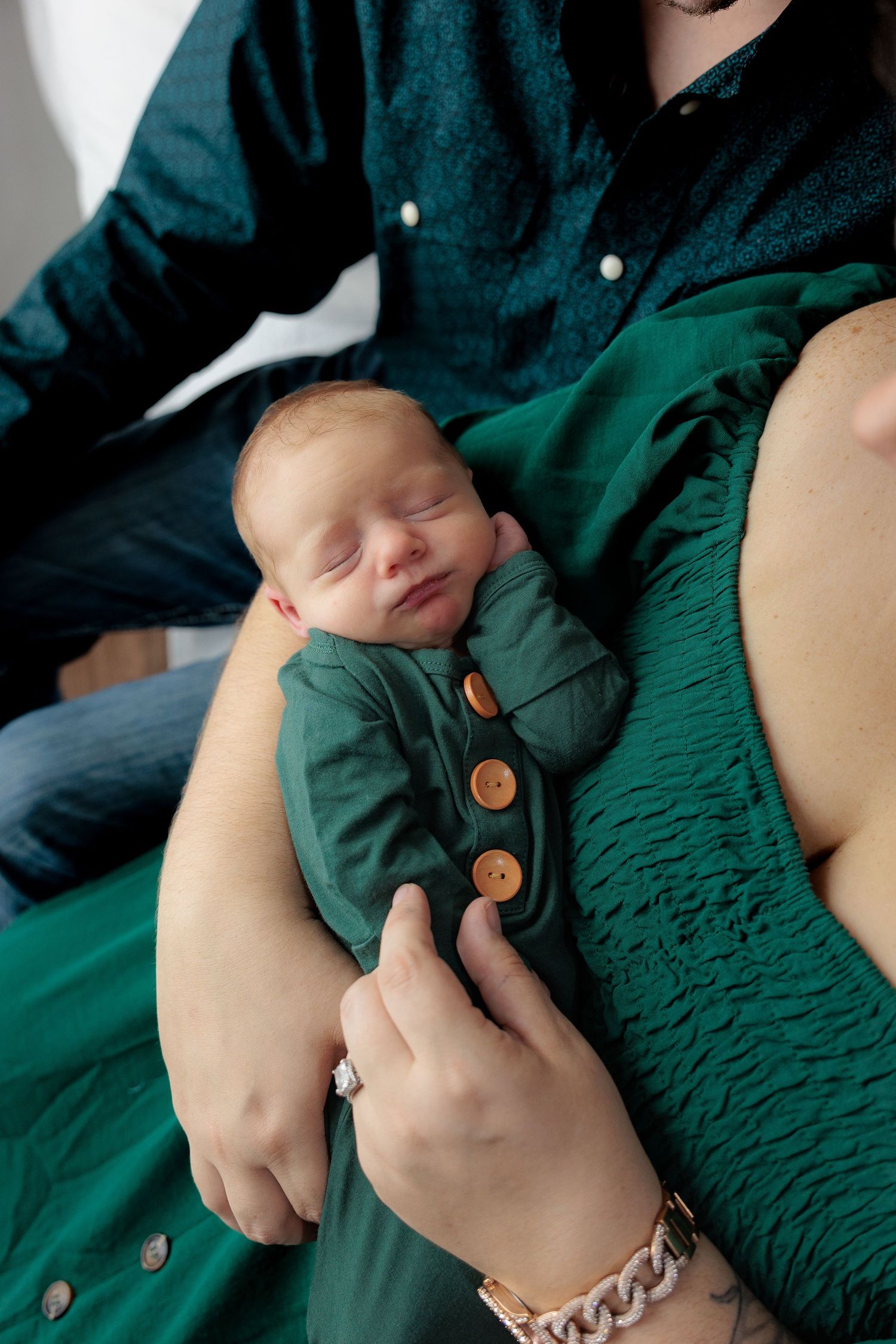 A series of hands holding and adjusting a green smocked dress with wooden buttons.