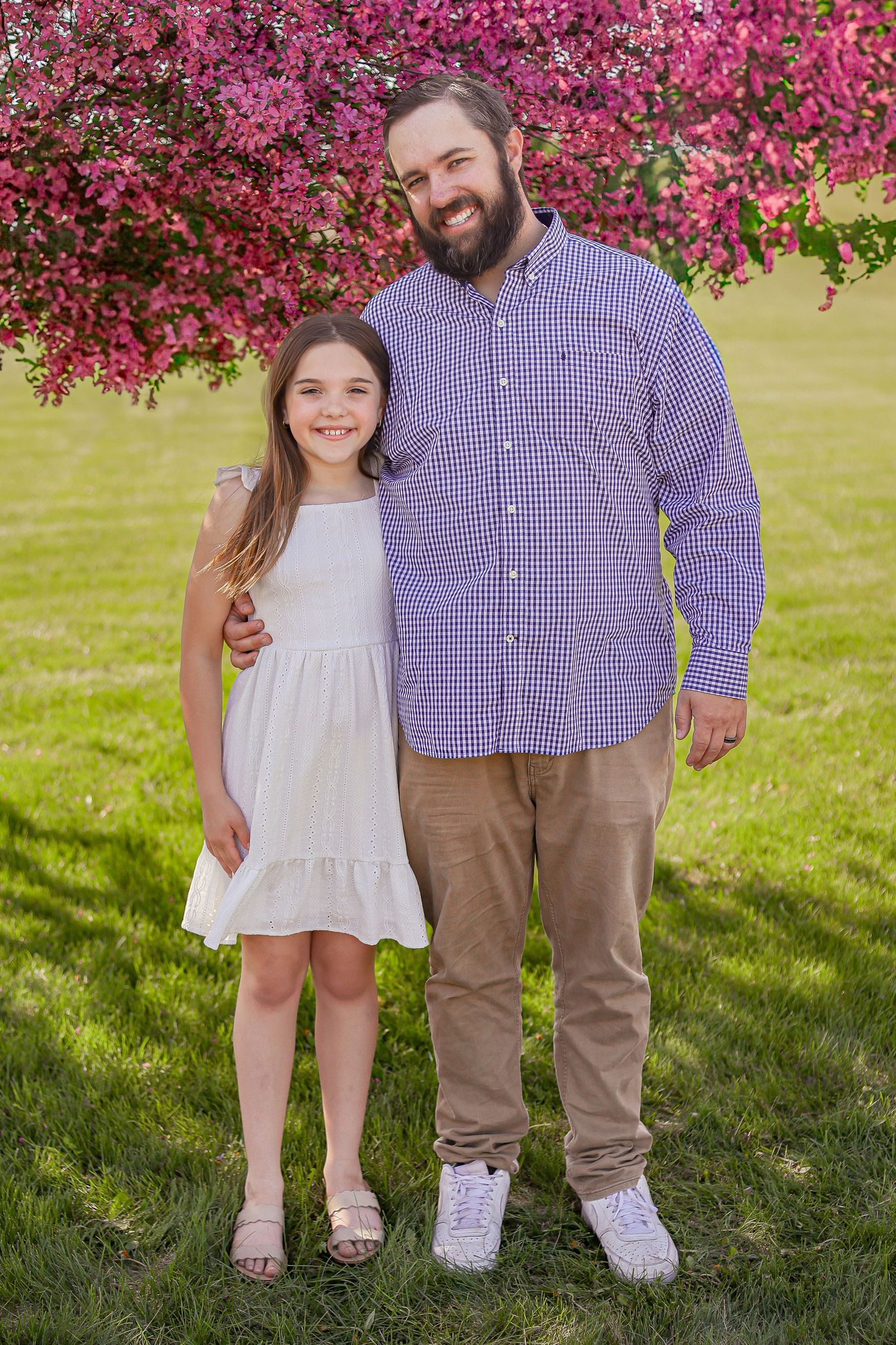 Family members in coordinated outfits pose together on grass beneath pink flowering trees.
