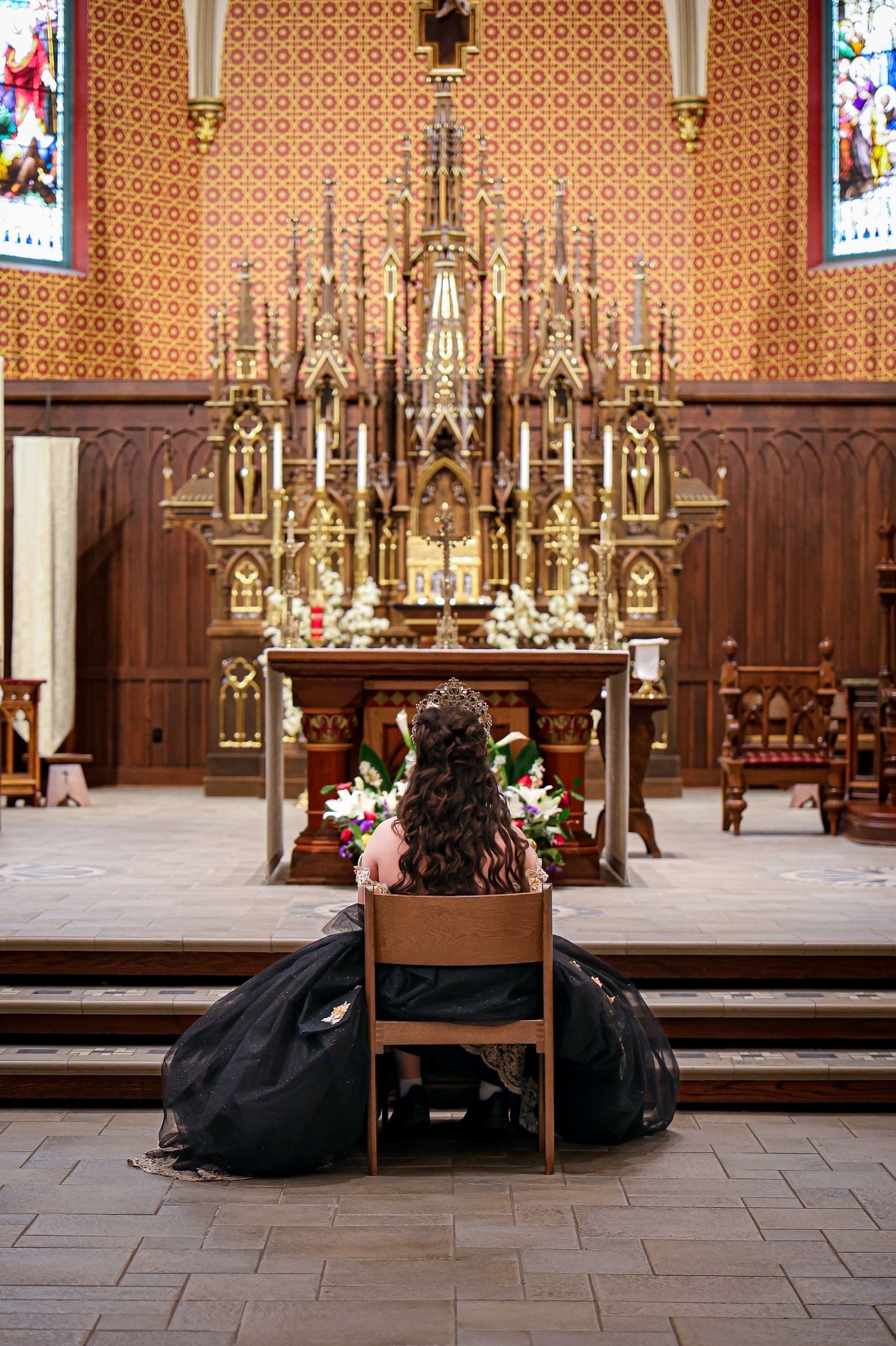 View of ornate golden church altar with person kneeling in black dress in foreground.