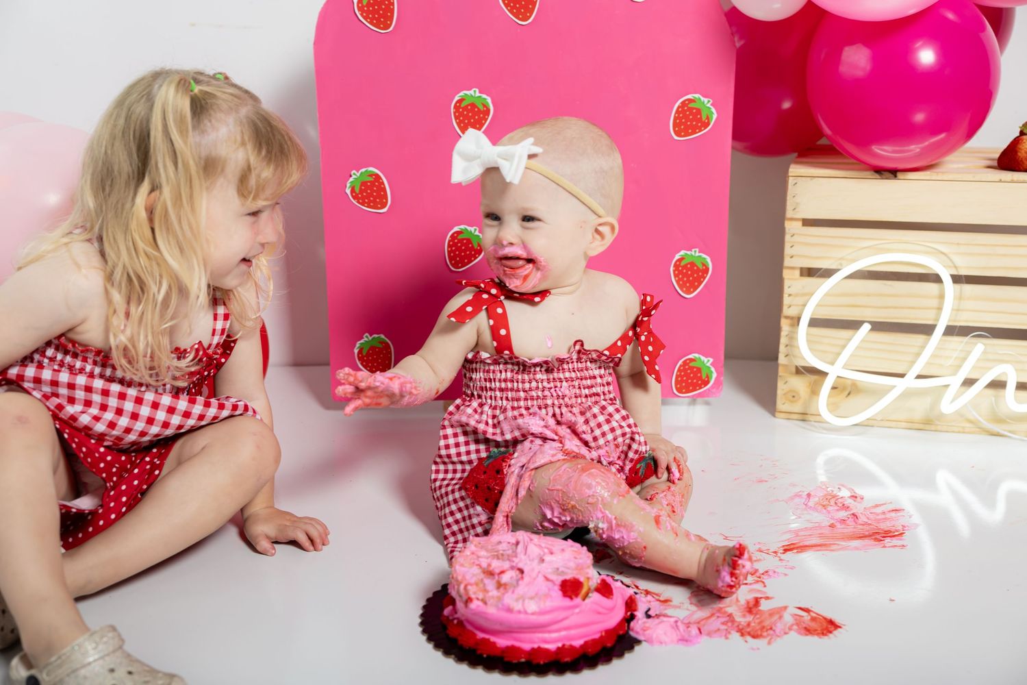 First birthday cake smash photo series with pink frosting and strawberry themed decorations.