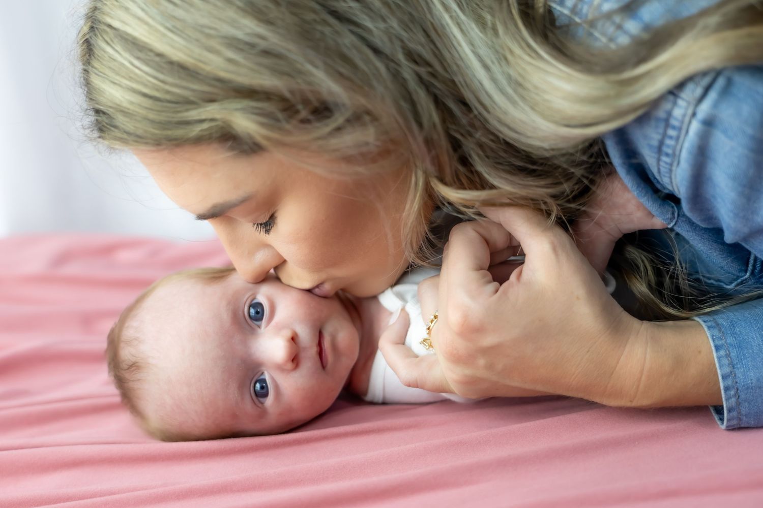 Sweet moment between parent and baby on pink bedding.
