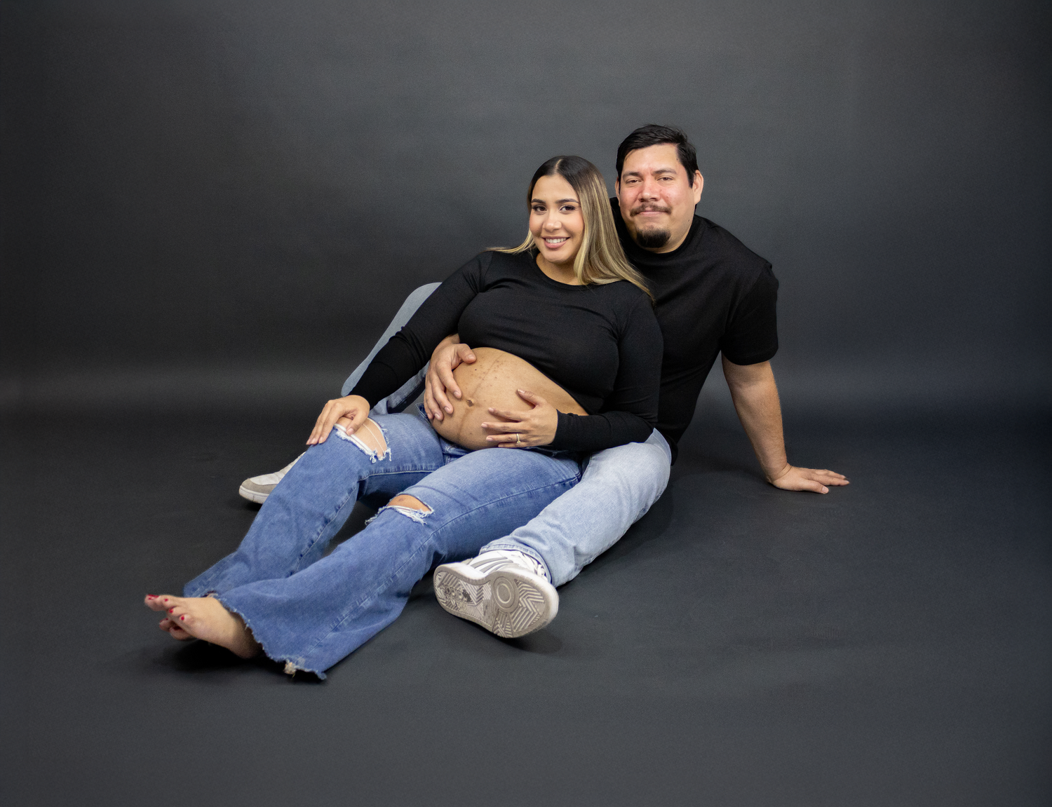 Intimate maternity photo series with couple posing on dark floor.