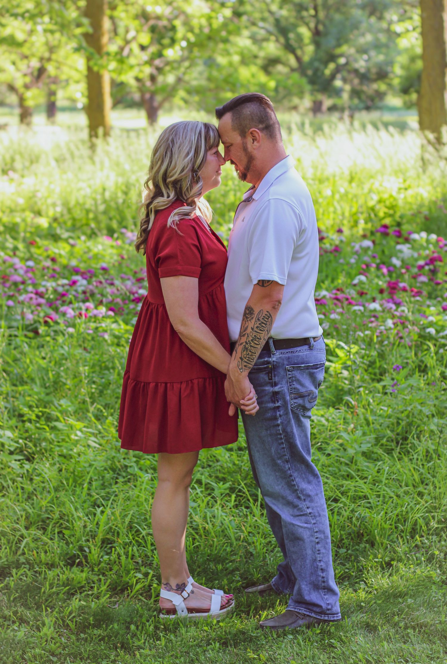 A tender moment between two people in a flowery garden setting wearing red dress and white shirt.