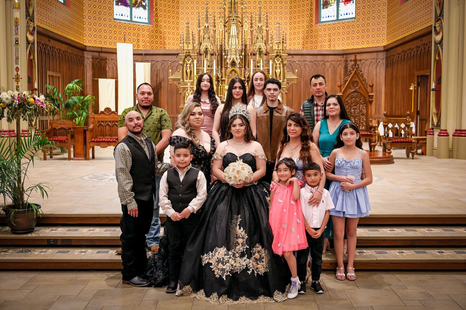 Wedding party gathered at the altar in a church with ornate gold chandelier and stained glass windows.