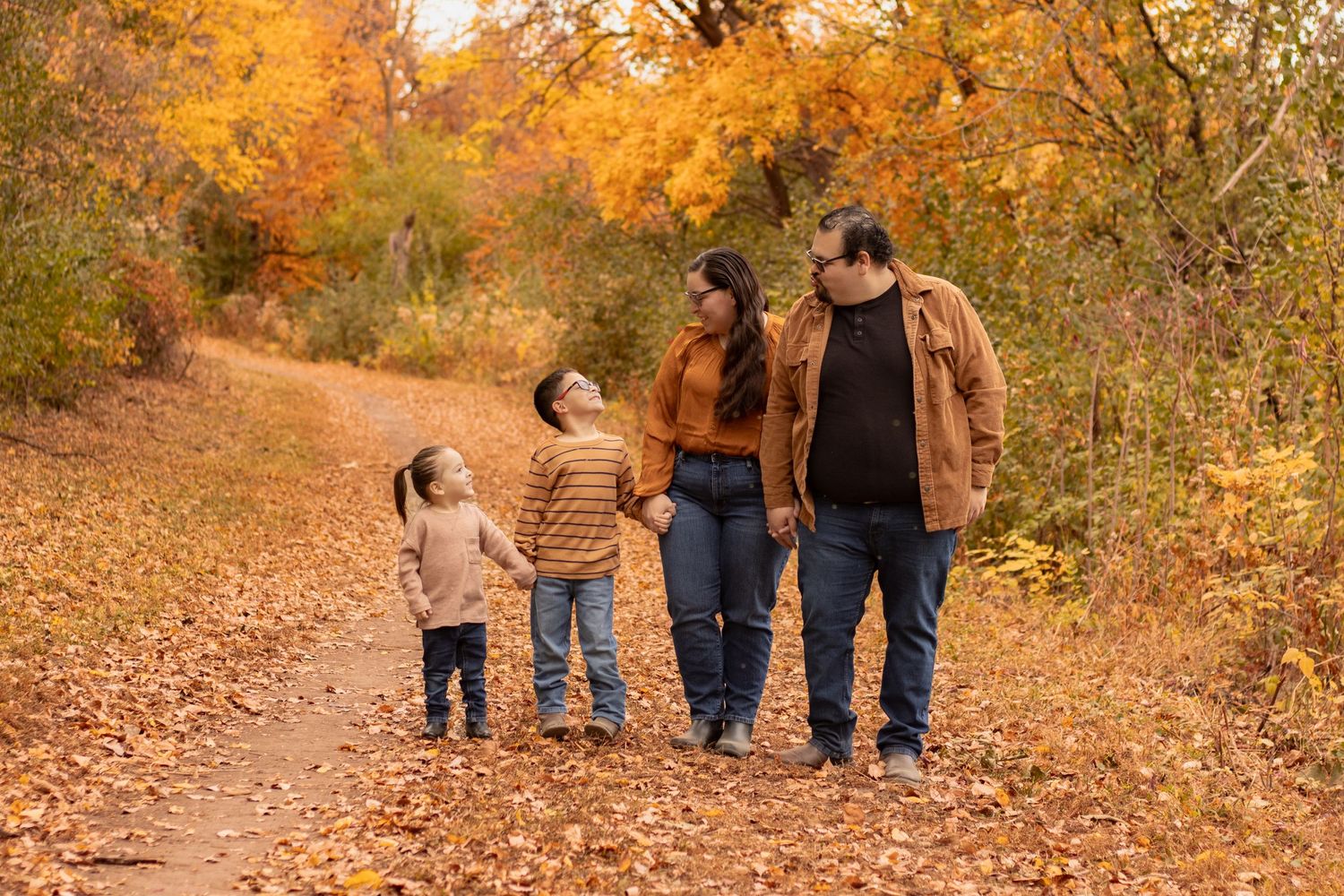 Family walking together on an autumn path covered in fallen orange and yellow leaves.